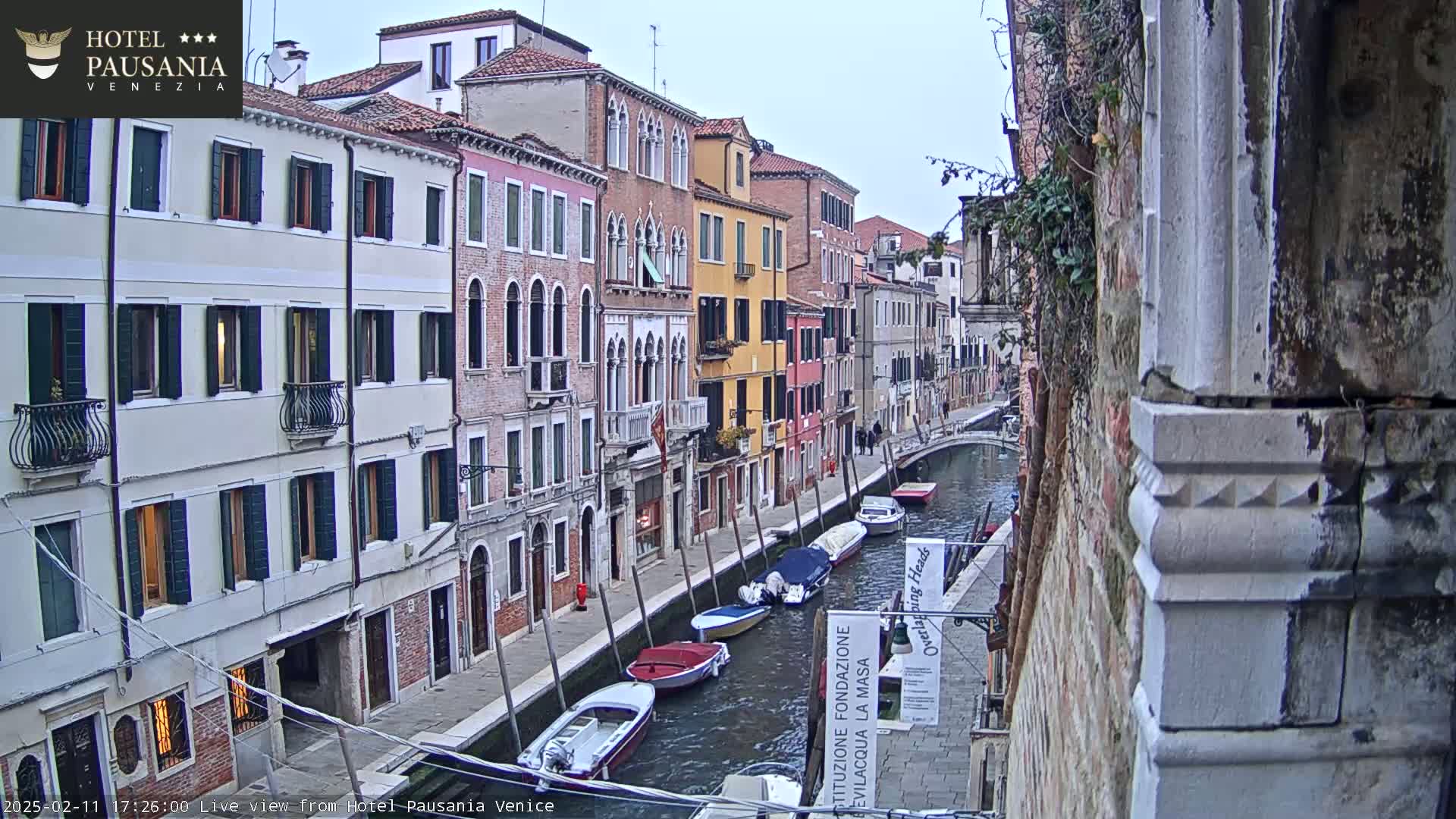 Several colorful buildings line a canal in Venice, where several boats are moored, under an overcast sky.