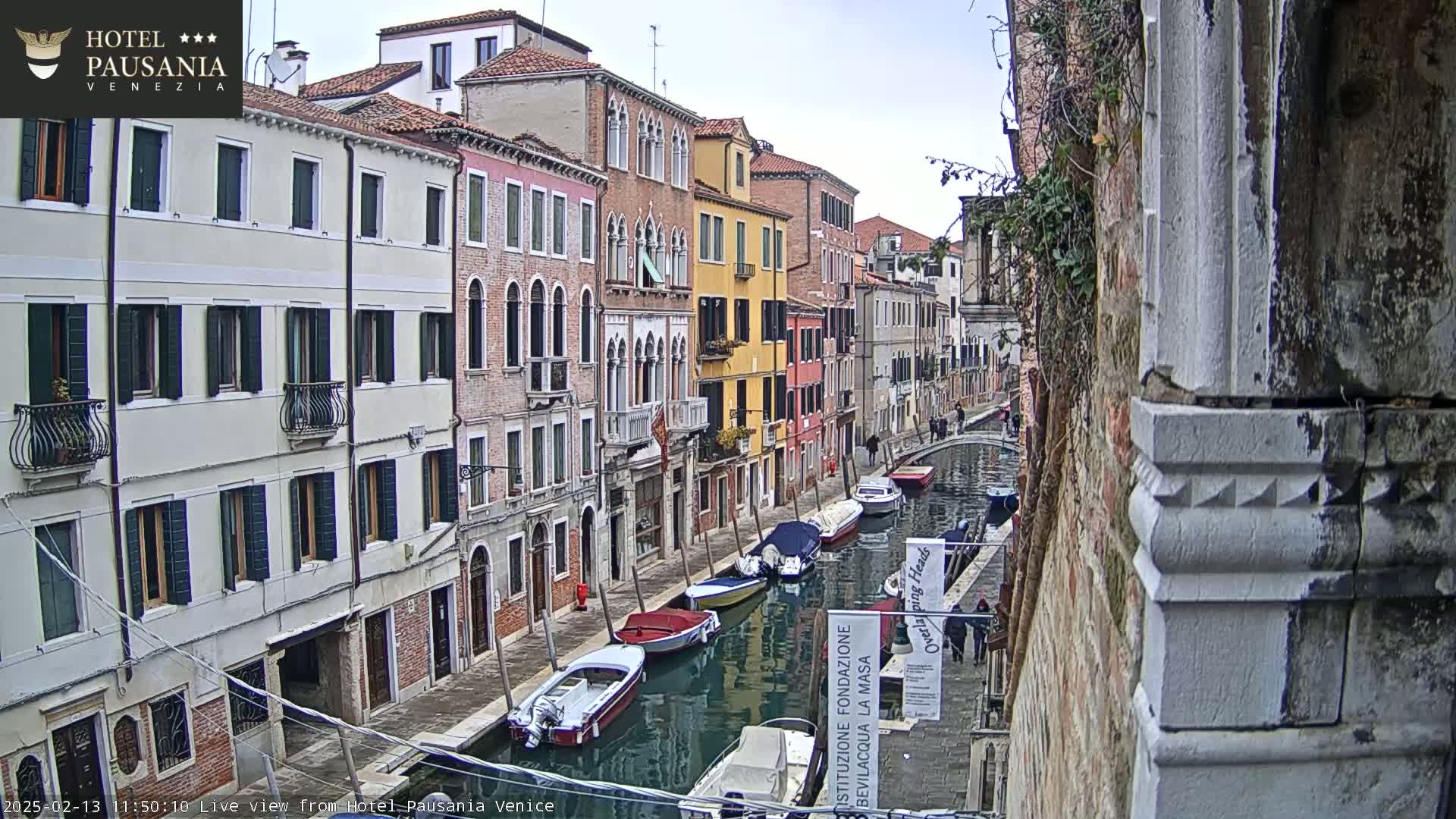 A narrow canal in Venice, Italy, is lined with colorful buildings under an overcast sky, with several boats moored along its banks.