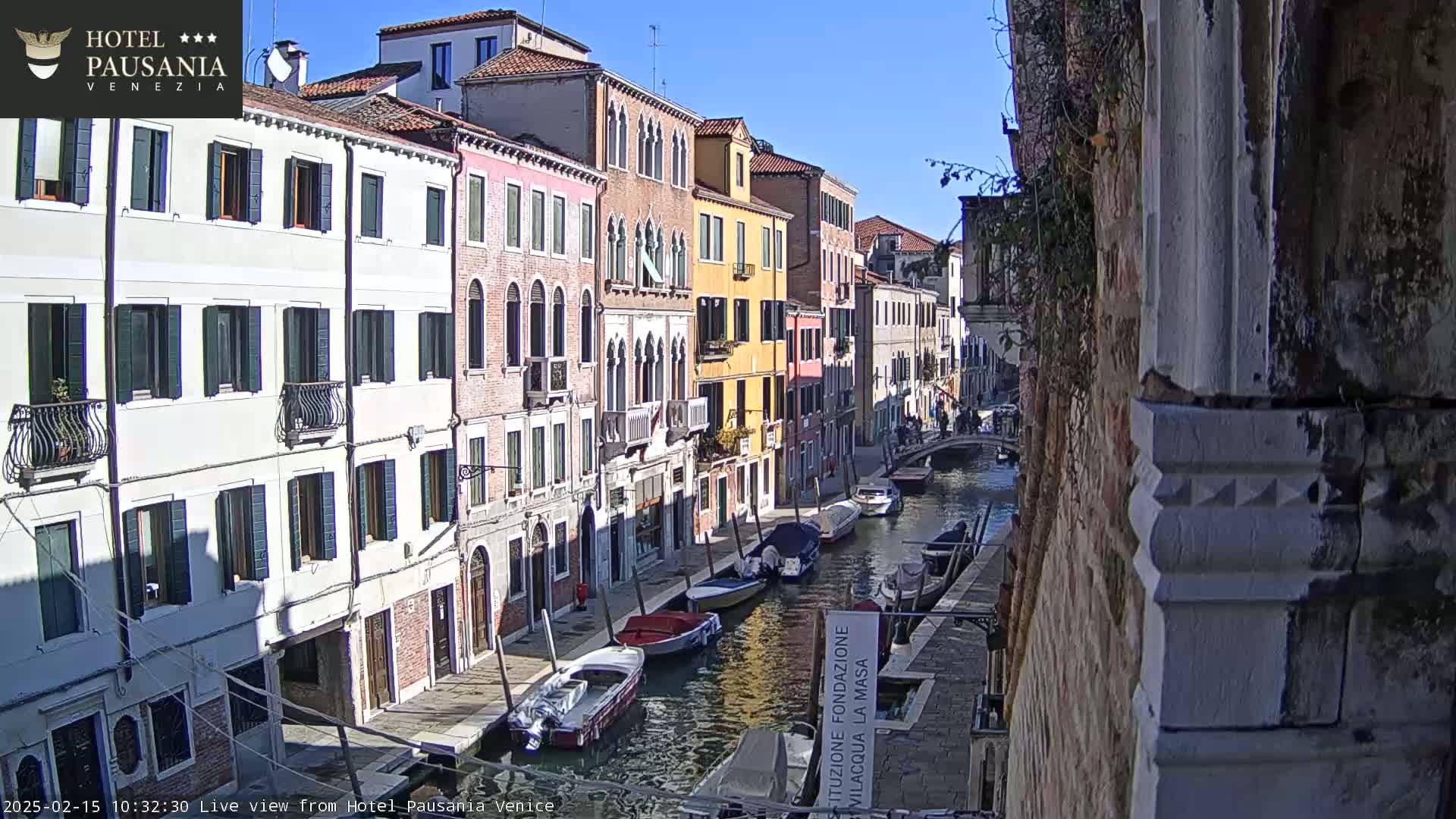 A sunny day in Venice shows several boats moored along a canal beside colorful buildings.