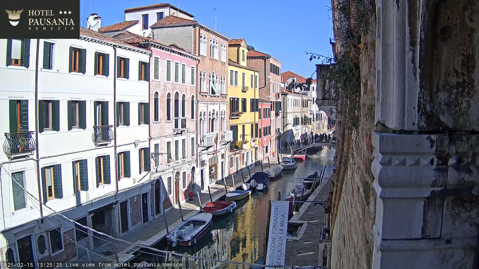 A sunny day in Venice shows several boats moored along a canal lined with colorful buildings.