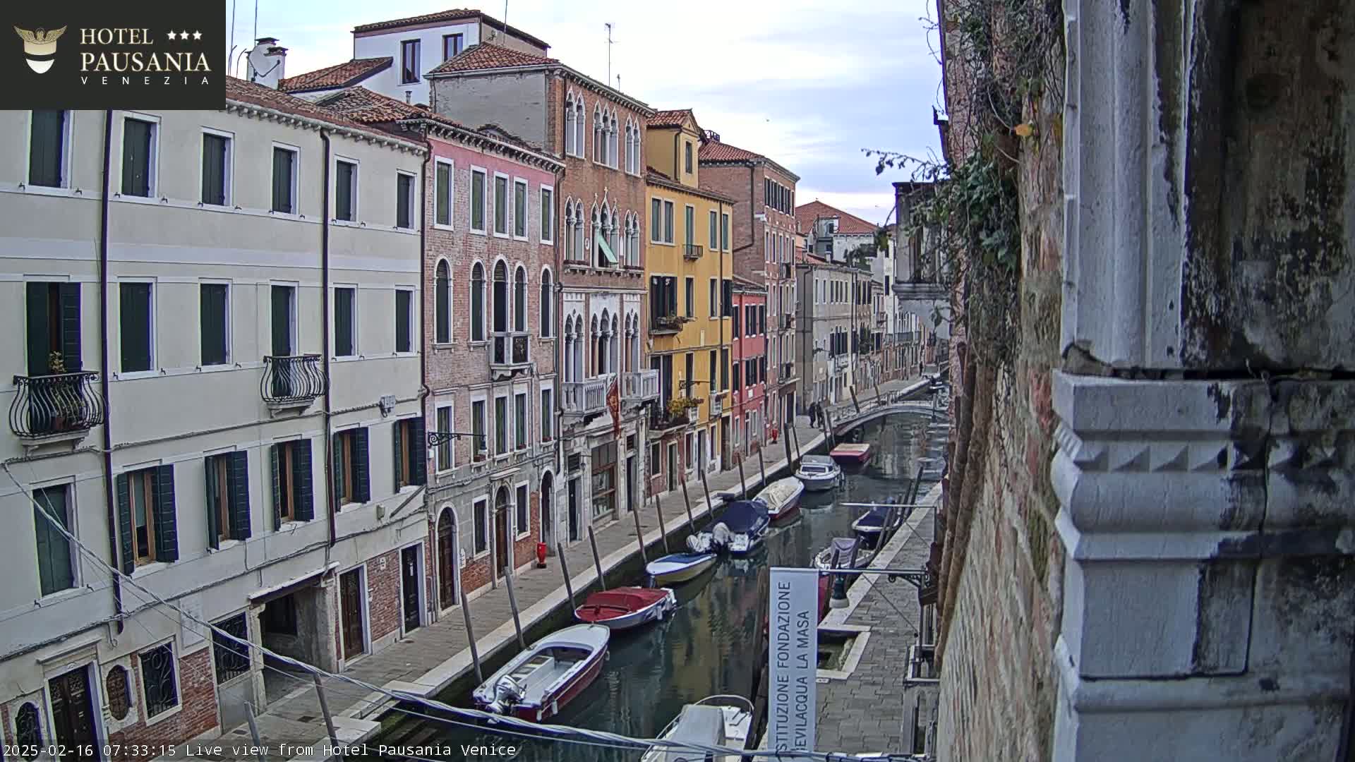 A canal in Venice, under an overcast sky, is lined with colorful buildings and several small boats moored along its banks.