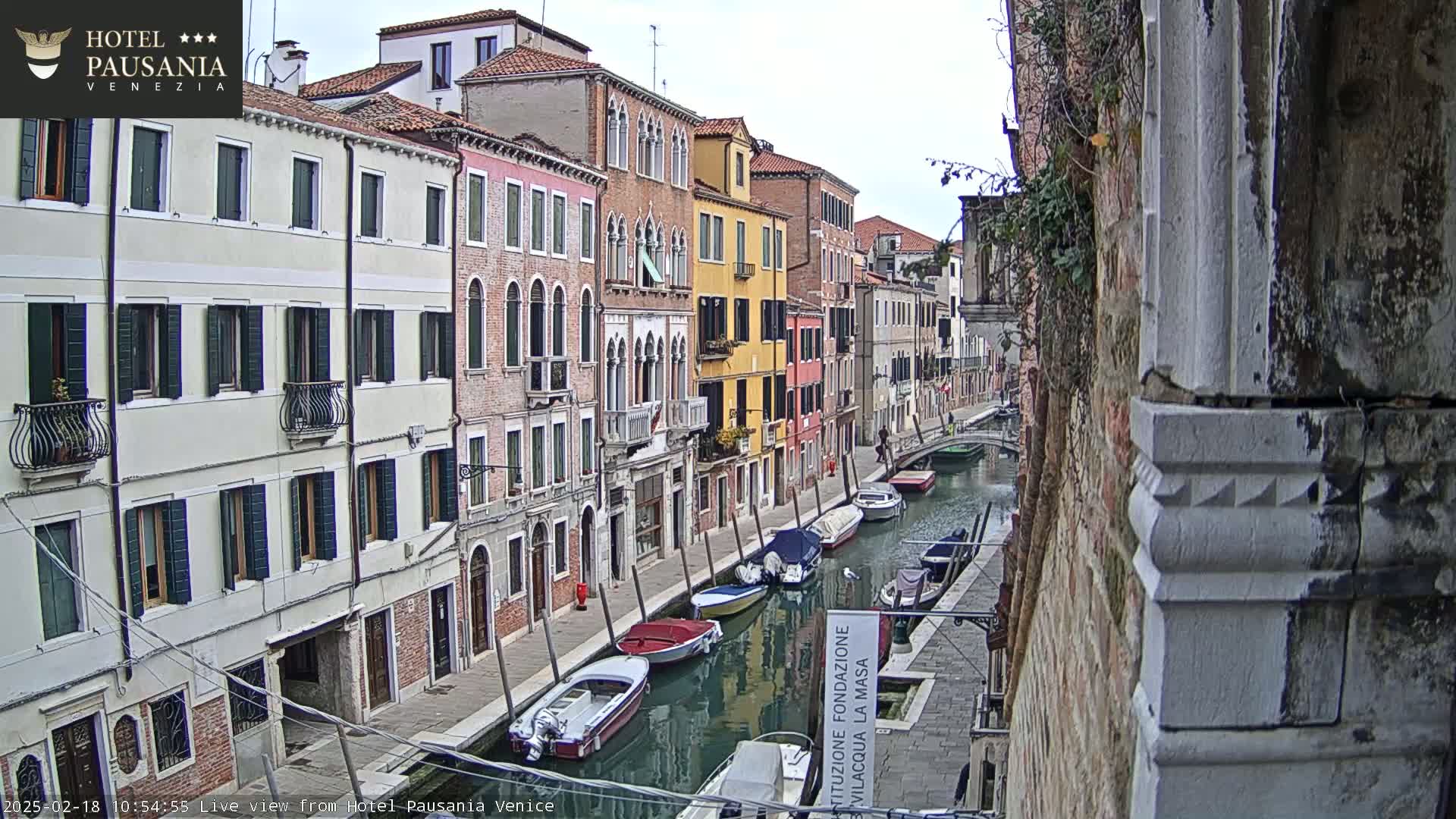 A canal in Venice, Italy, lined with colorful buildings on a cloudy day, shows several boats moored along its banks.