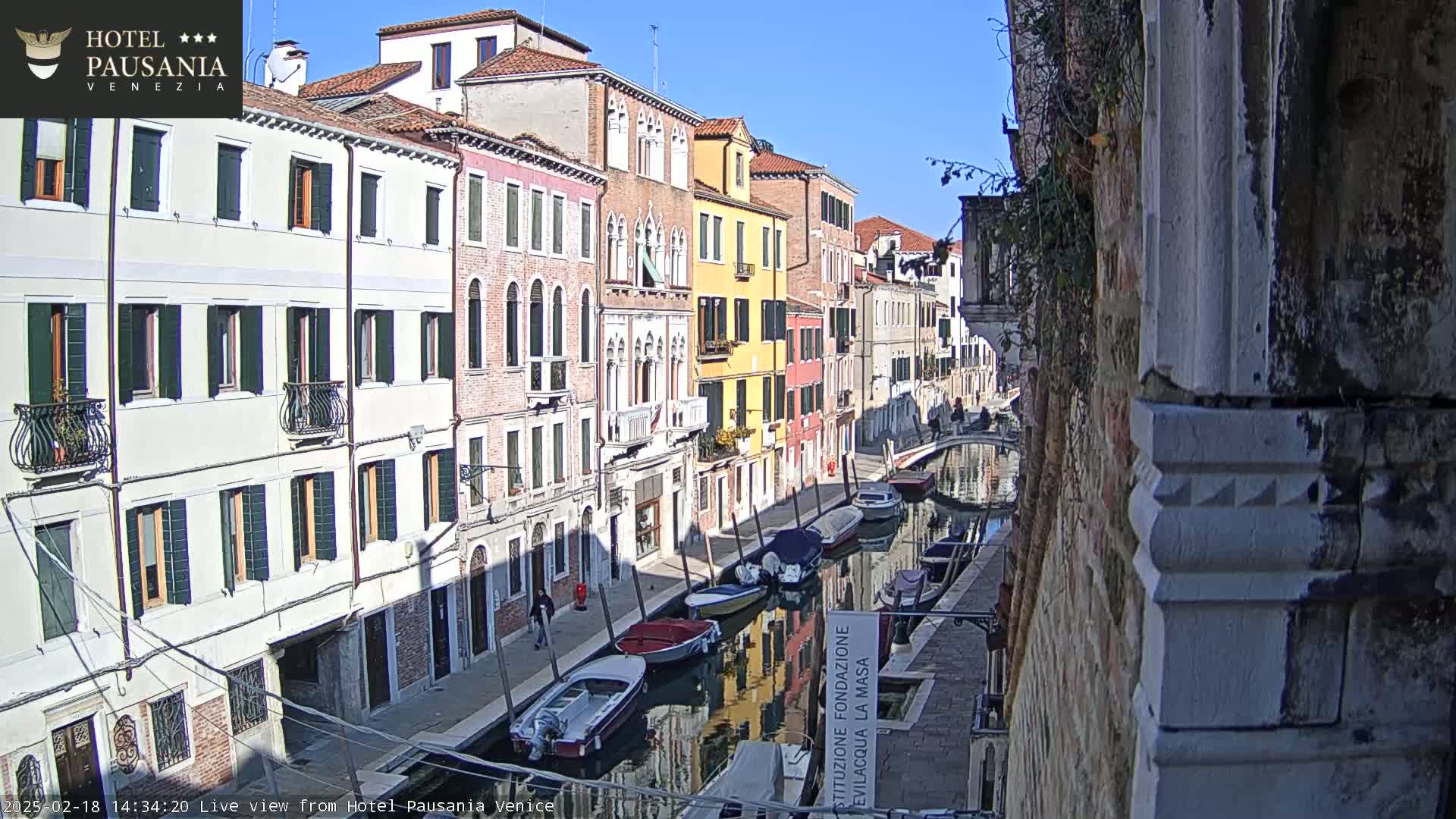 A sunny day in Venice, showing a canal lined with colorful buildings and several moored boats.