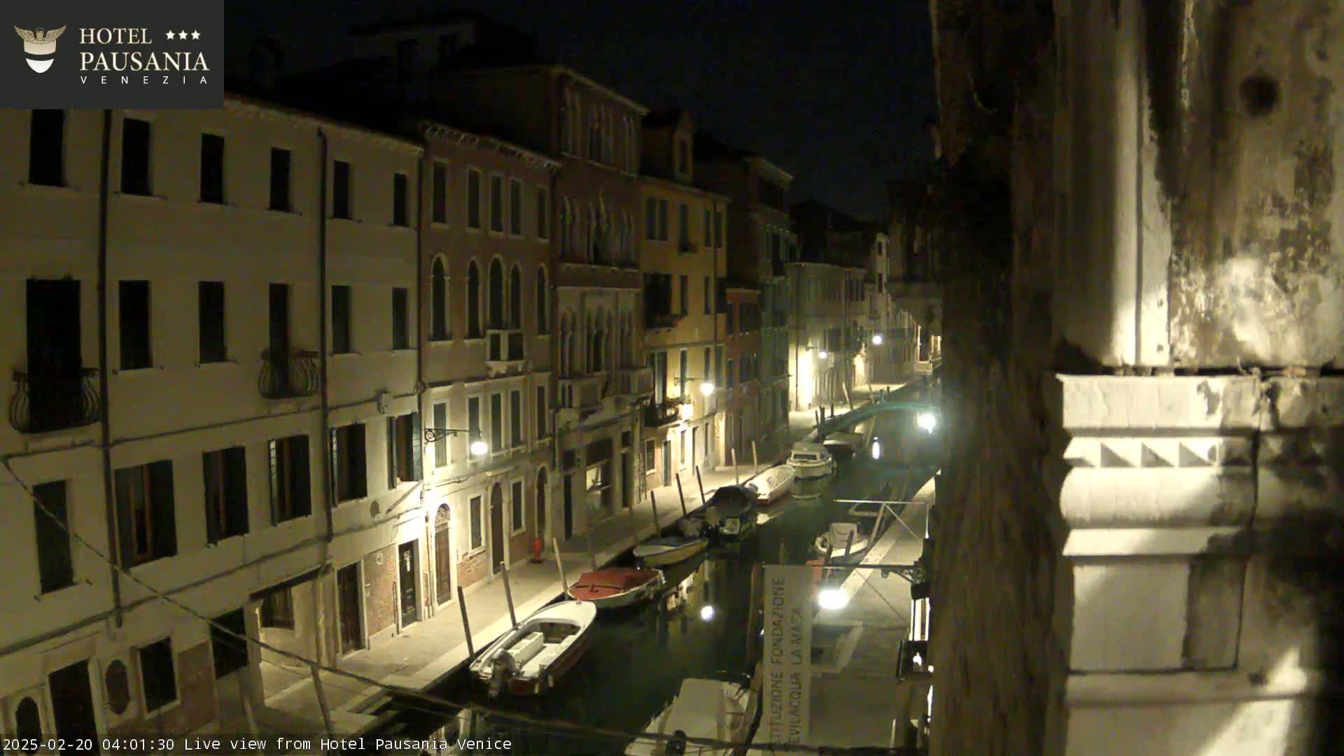 A nighttime view of a canal in Venice, Italy, lined with illuminated buildings and several moored boats.