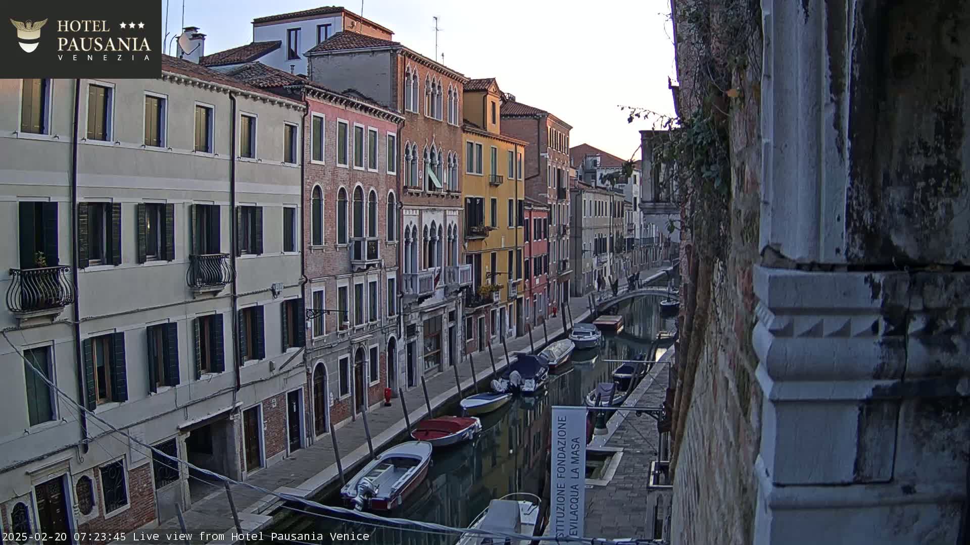 A narrow Venetian canal, lined with colorful buildings, is partially visible under a clear, dawn sky; several boats are moored along the waterway.