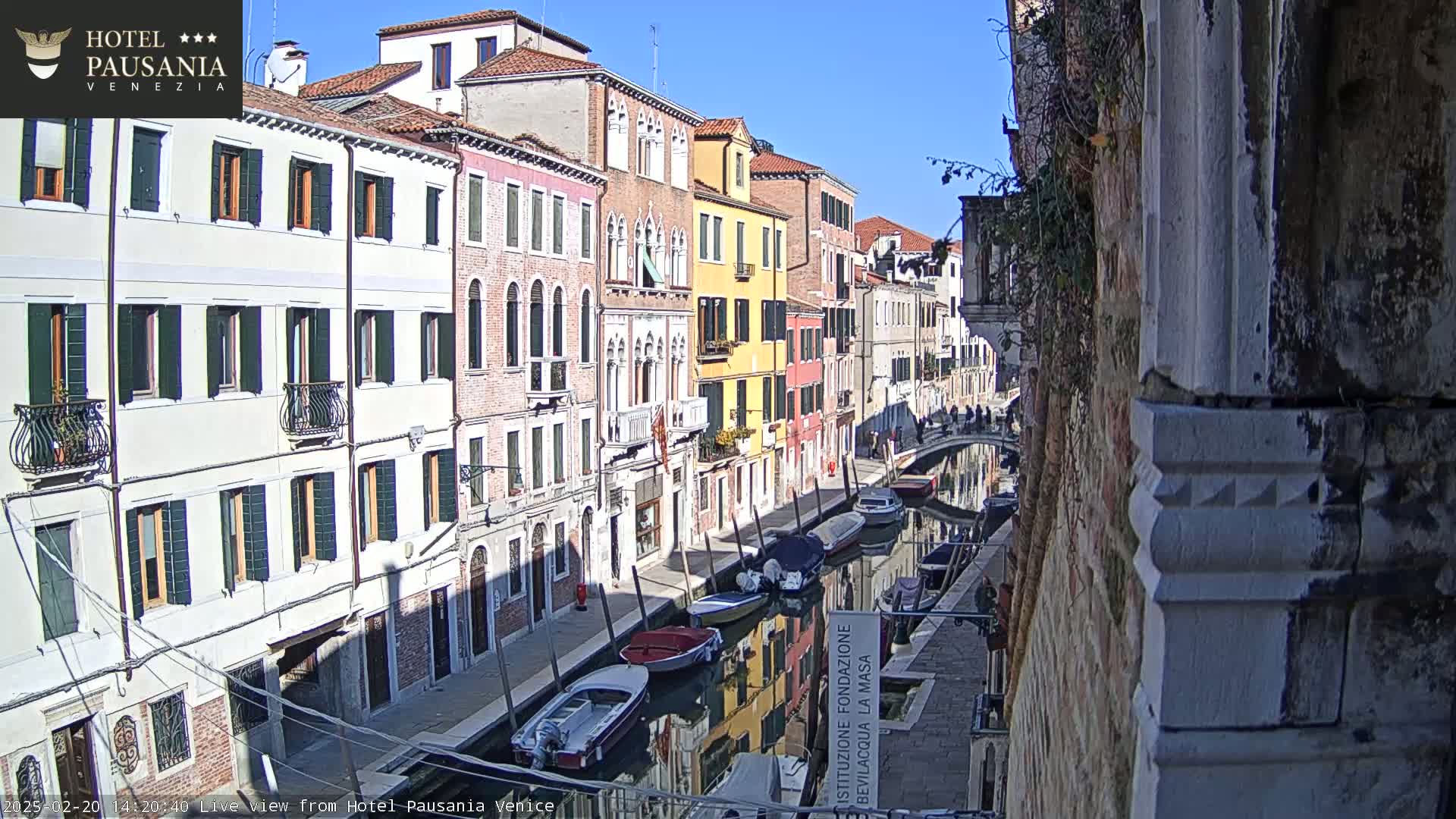A sunny day in Venice shows a canal with several boats moored along its sides, lined with colorful buildings.