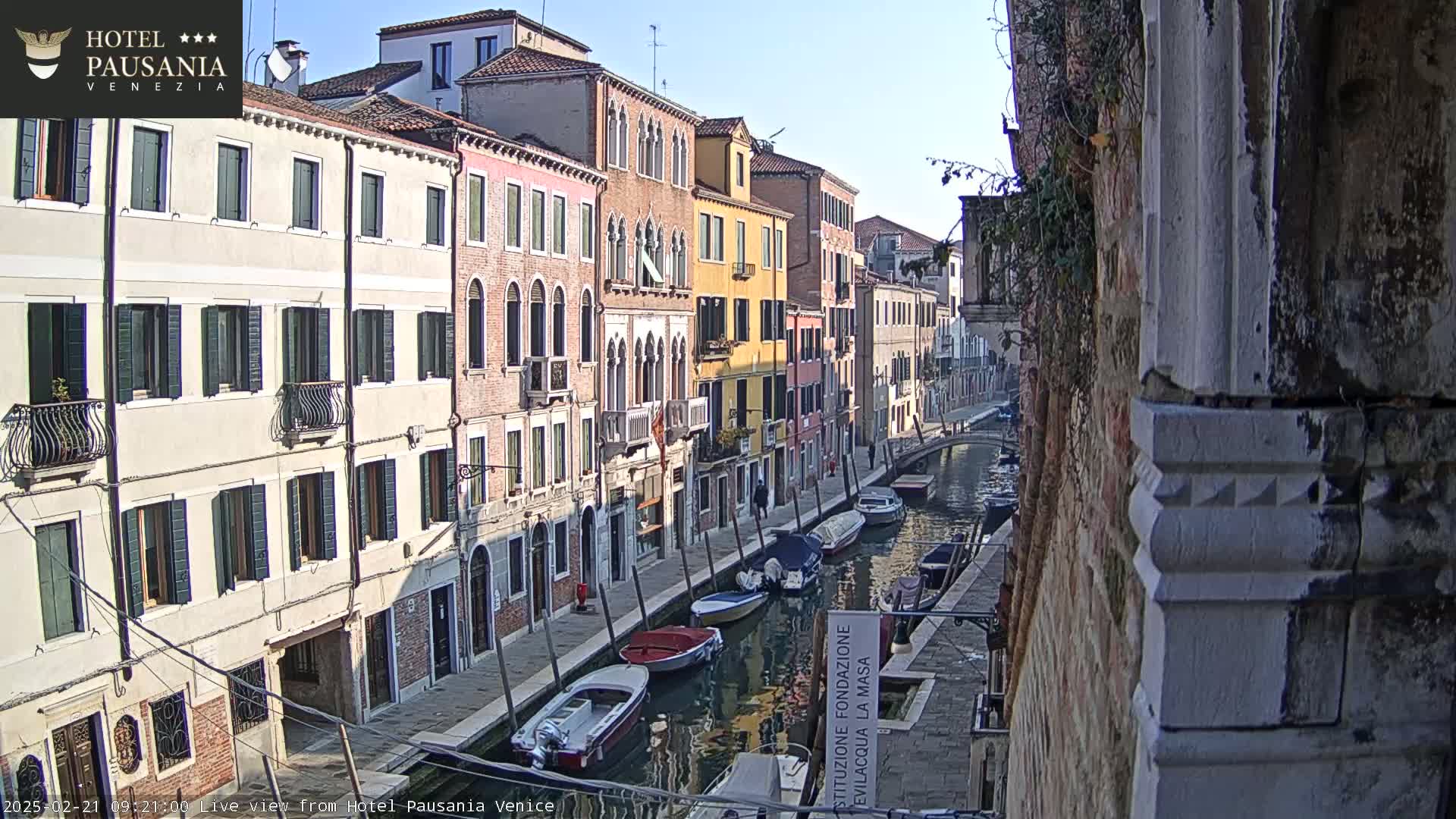 A sunny day in Venice shows a canal lined with colorful buildings and several boats moored along its banks.