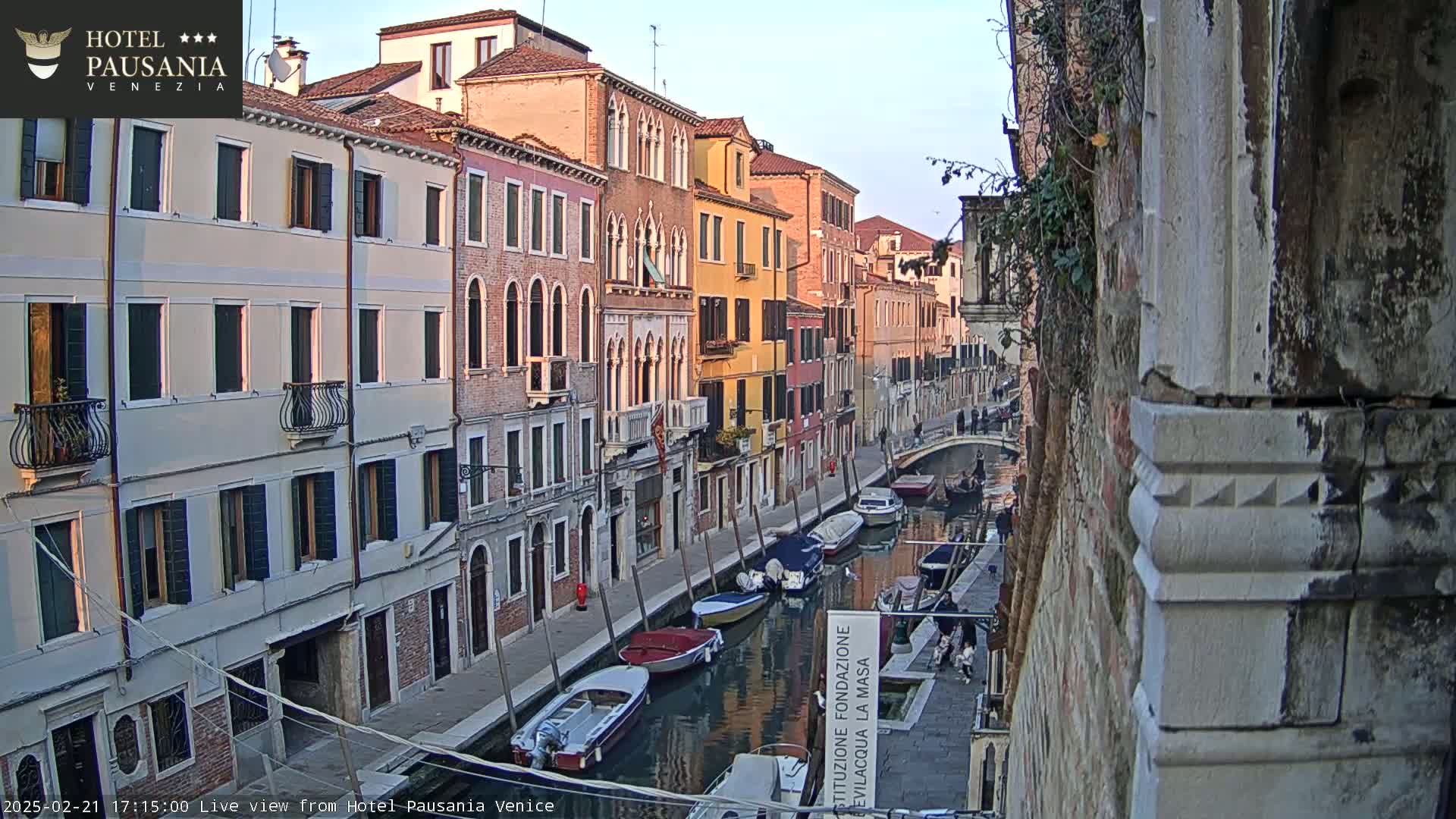 Several colorful buildings line a narrow canal in Venice, Italy, under a clear, twilight sky, with several boats moored along the waterway.