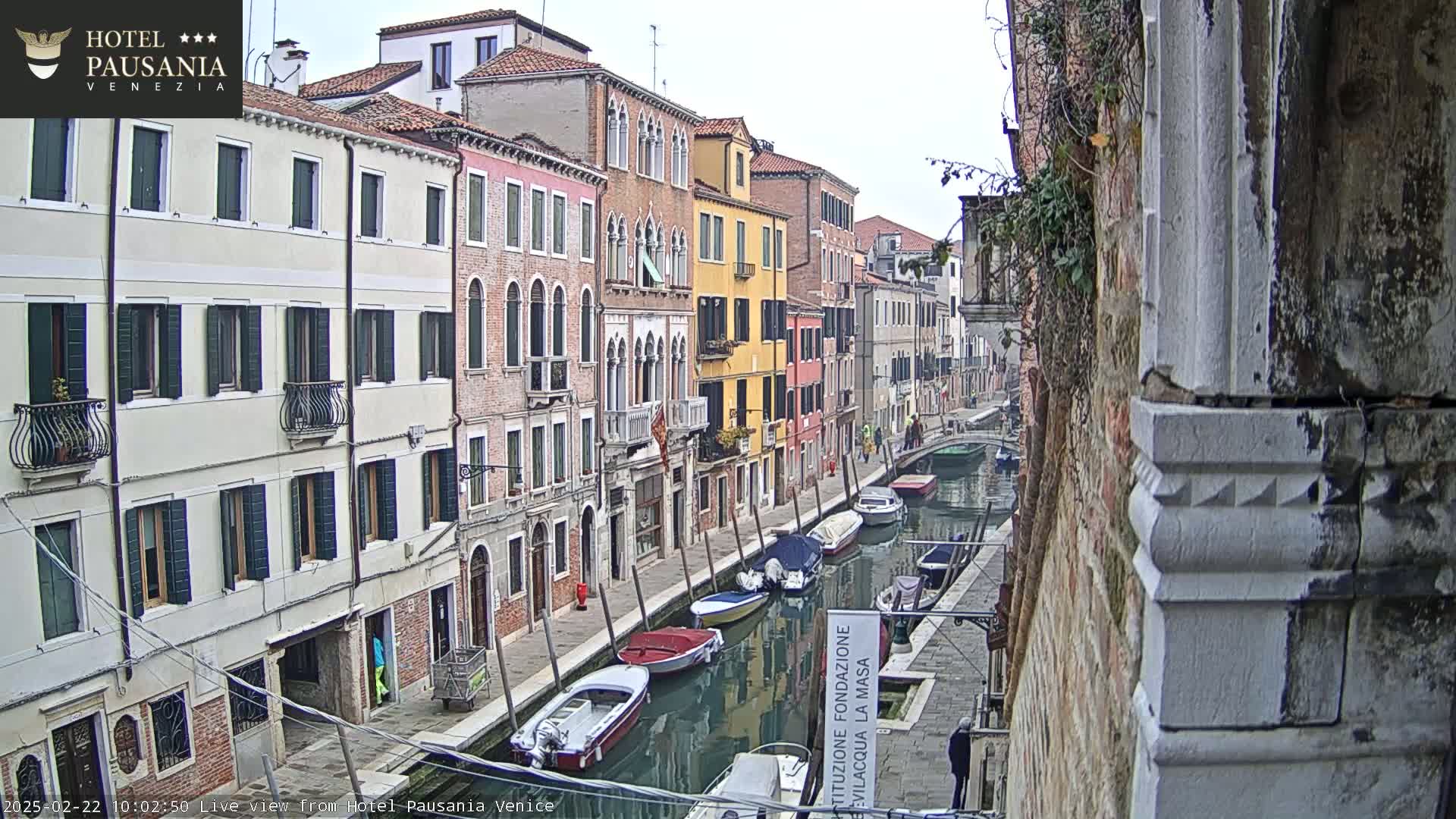 A canal in Venice, Italy, is lined with colorful buildings on an overcast day; several small boats are moored along the waterway.
