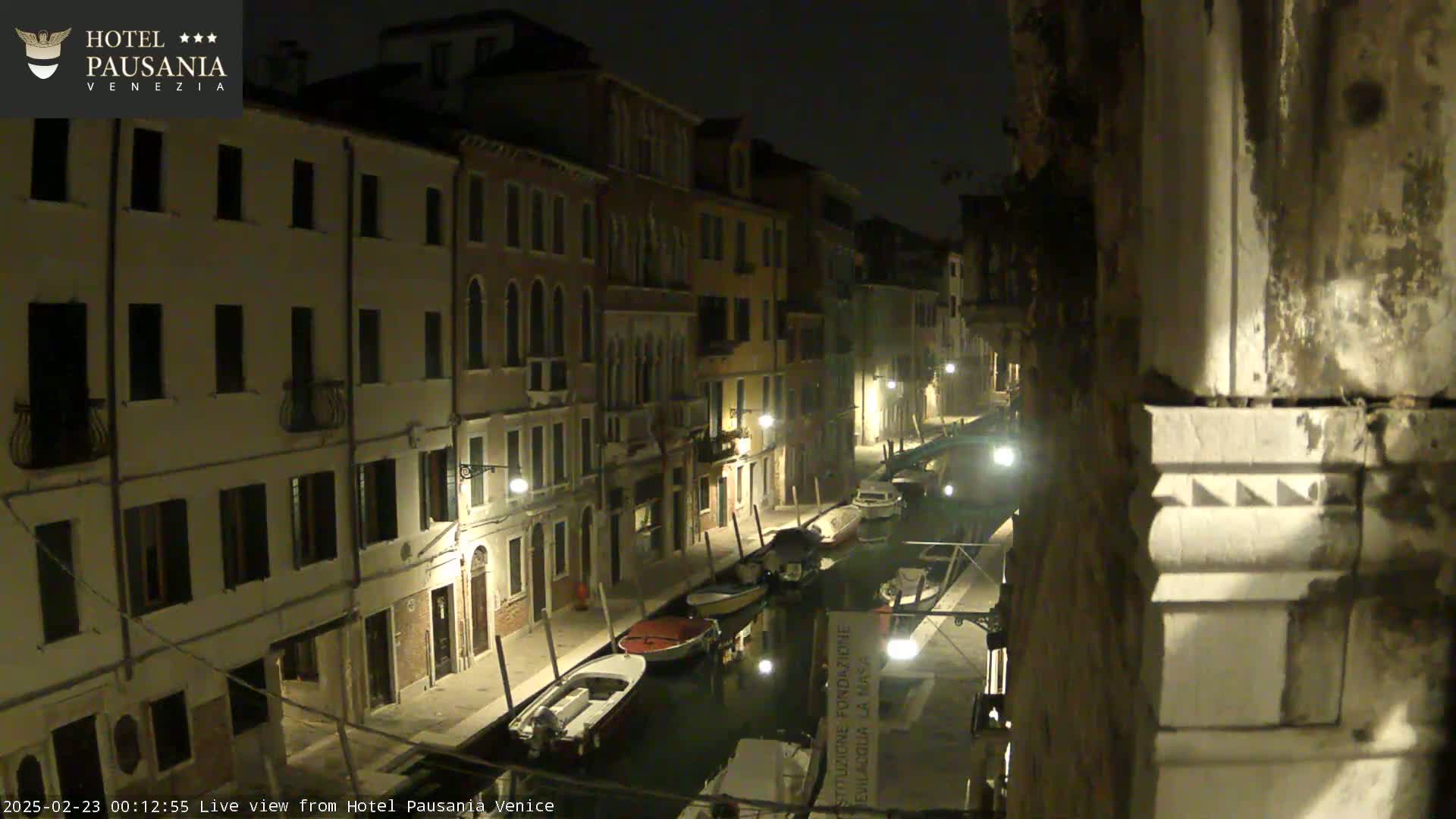 A nighttime view of a canal in Venice, Italy, lined with buildings and several moored boats.