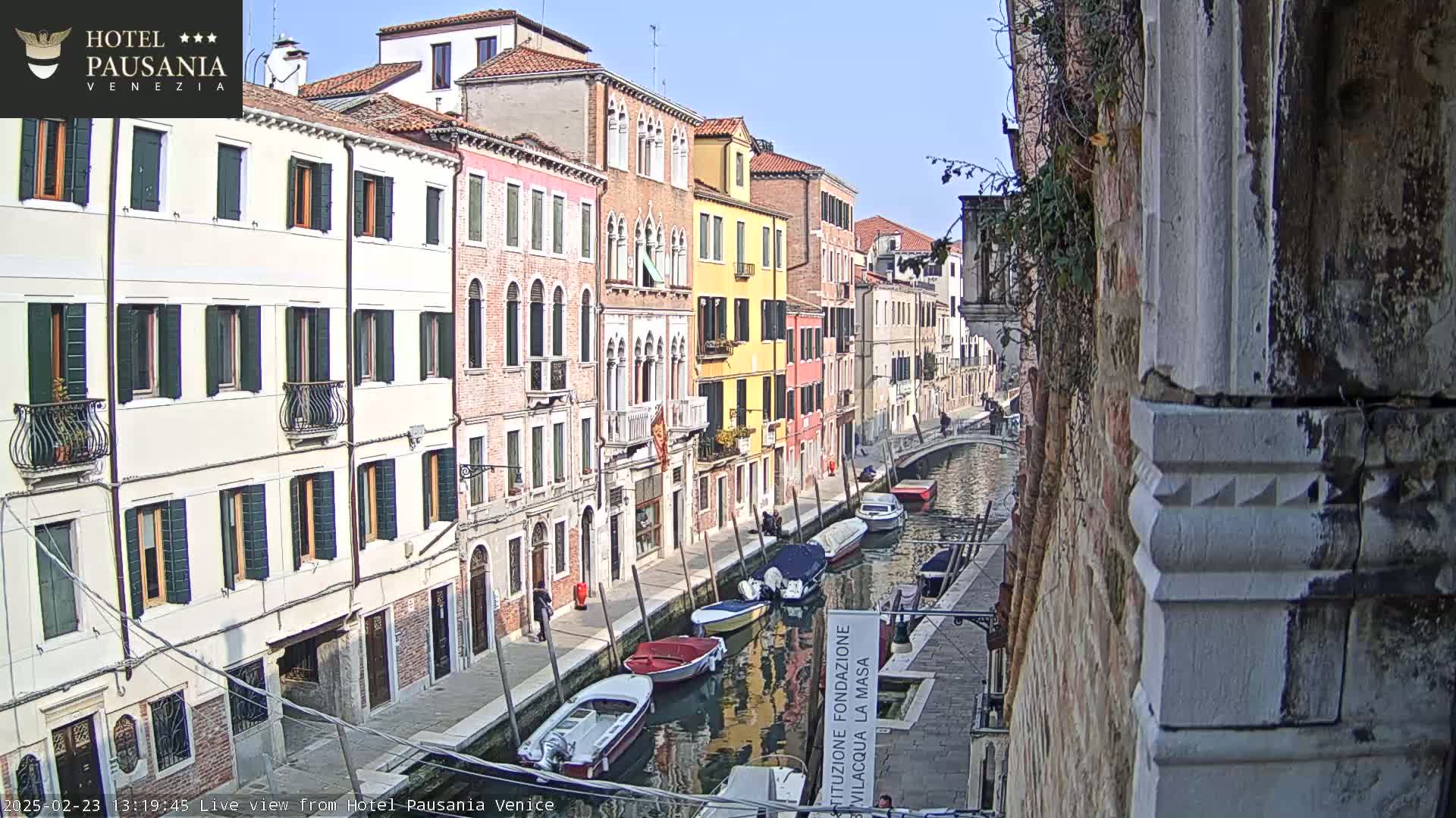 A sunny day in Venice, showing colorful buildings lining a canal with several boats moored along its sides.