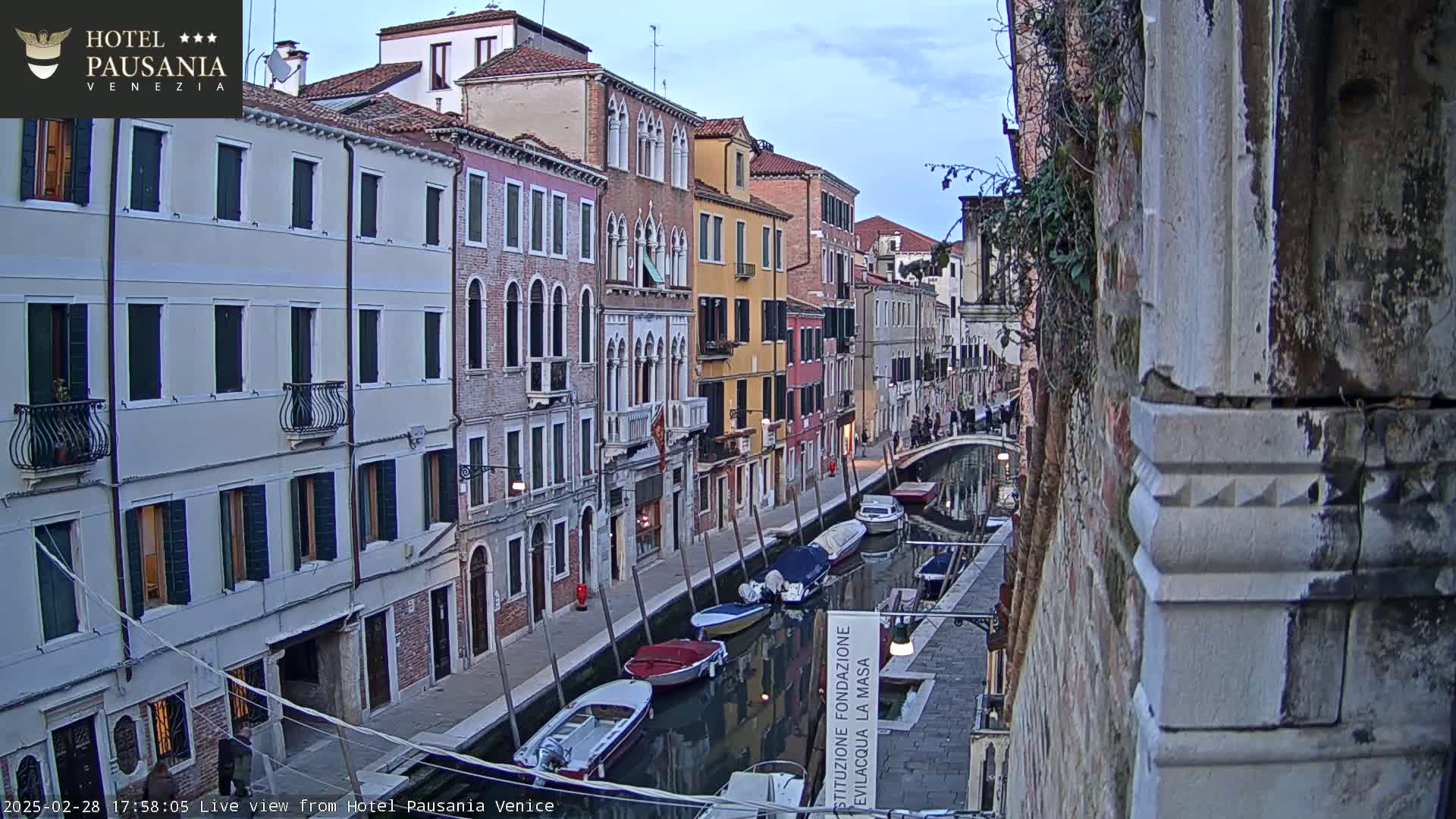 A narrow Venetian canal at dusk, lined with colorful buildings and several moored boats.