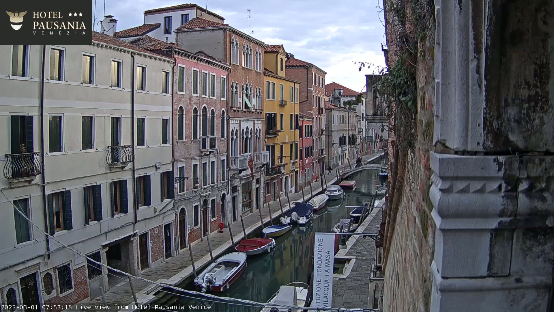 A canal in Venice, under an overcast sky, is lined with colorful buildings and several moored boats.