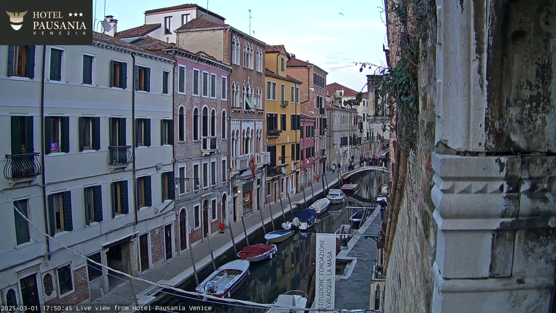 A canal in Venice, Italy, lined with closely-packed buildings, is filled with several boats under a twilight sky.