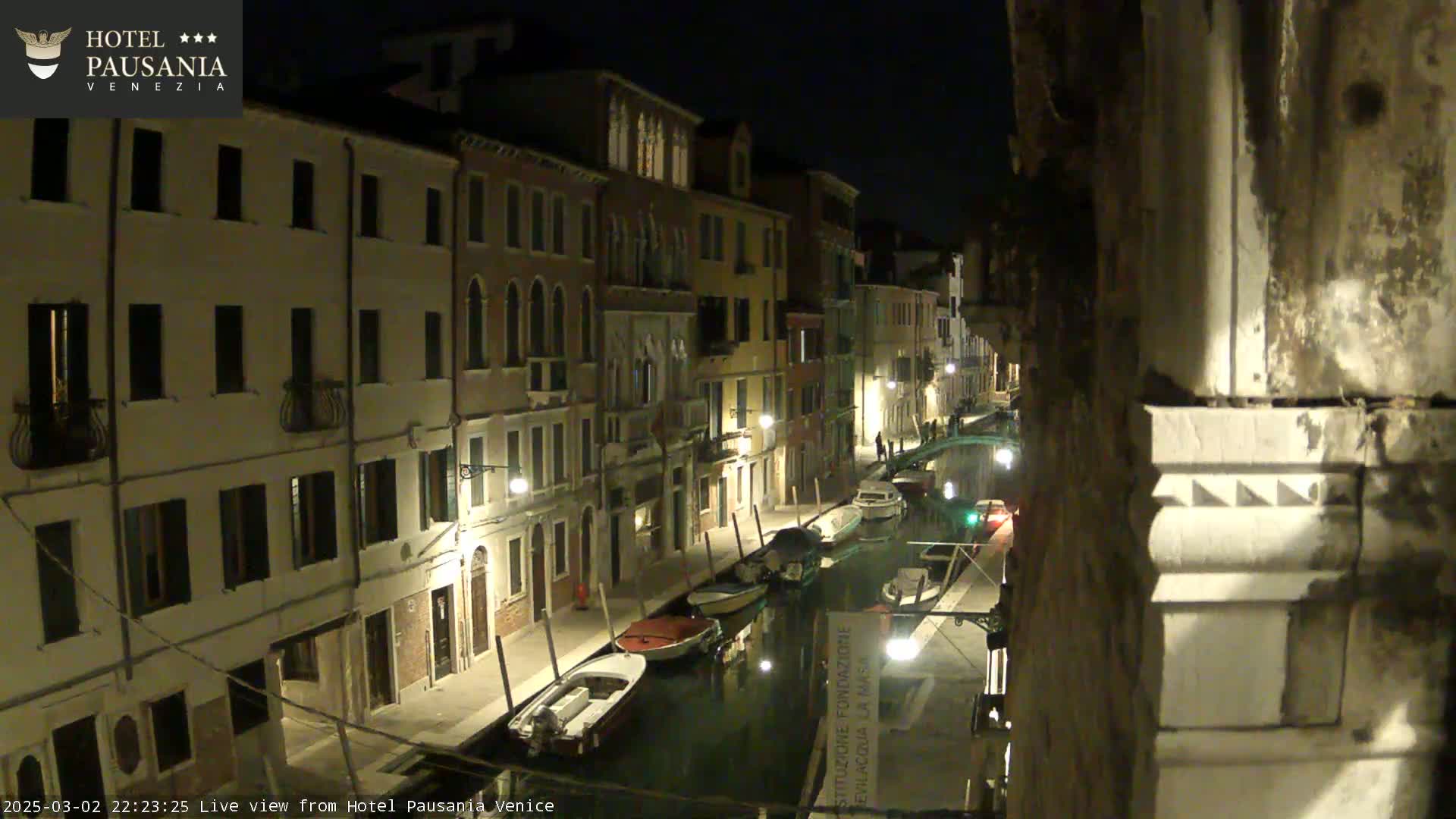 A nighttime view of a canal in Venice, lined with illuminated buildings and moored boats.
