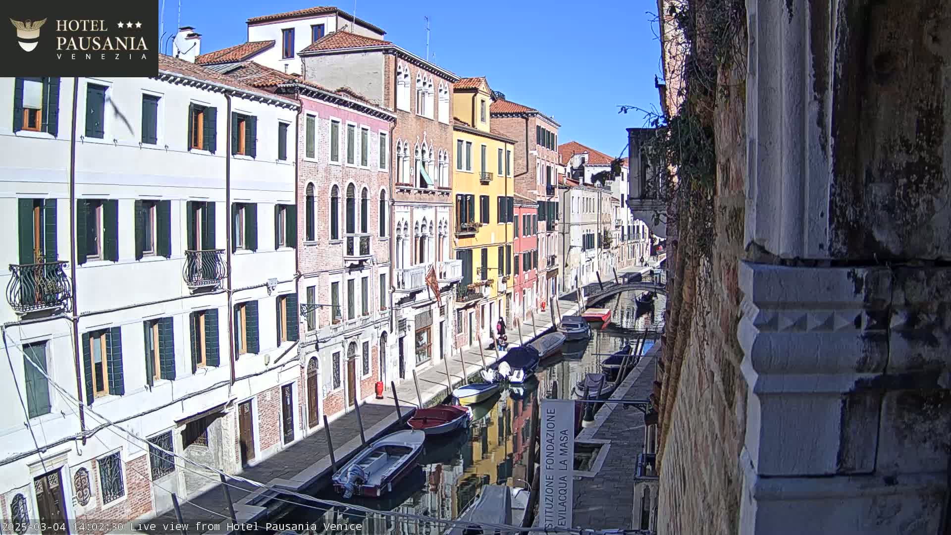 A sunny day in Venice shows colorful buildings lining a canal with several boats moored along the waterway.