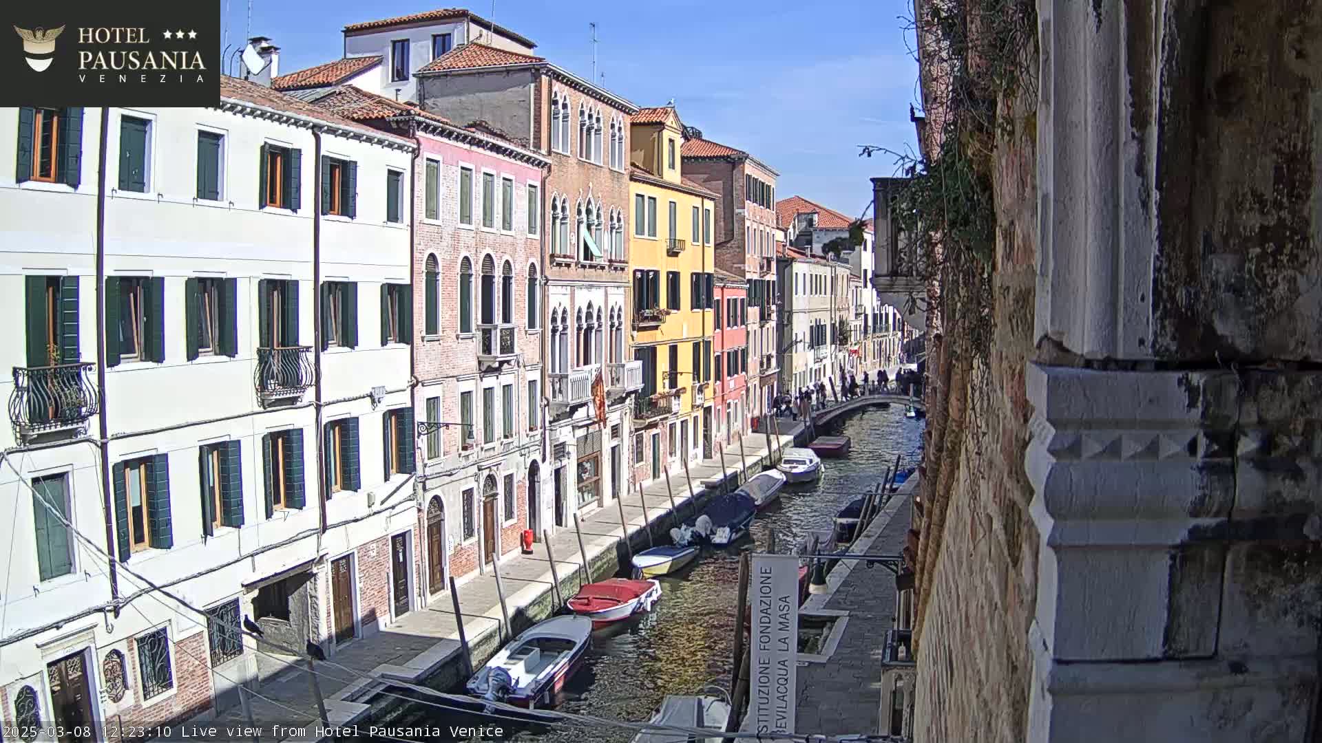 A sunny day in Venice shows several colorful buildings lining a canal where several boats are moored.