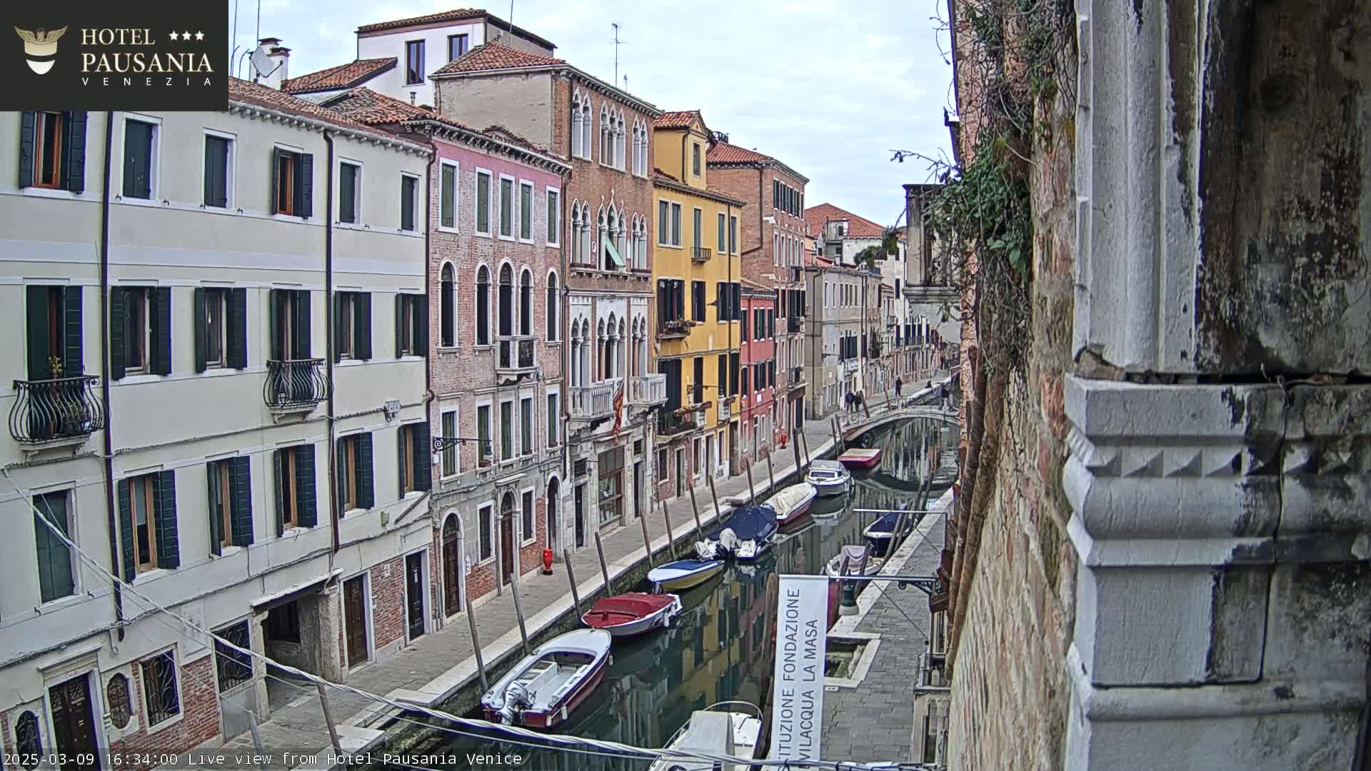 A canal in Venice, Italy, lined with colorful buildings on a cloudy day, features several small boats moored along its banks.