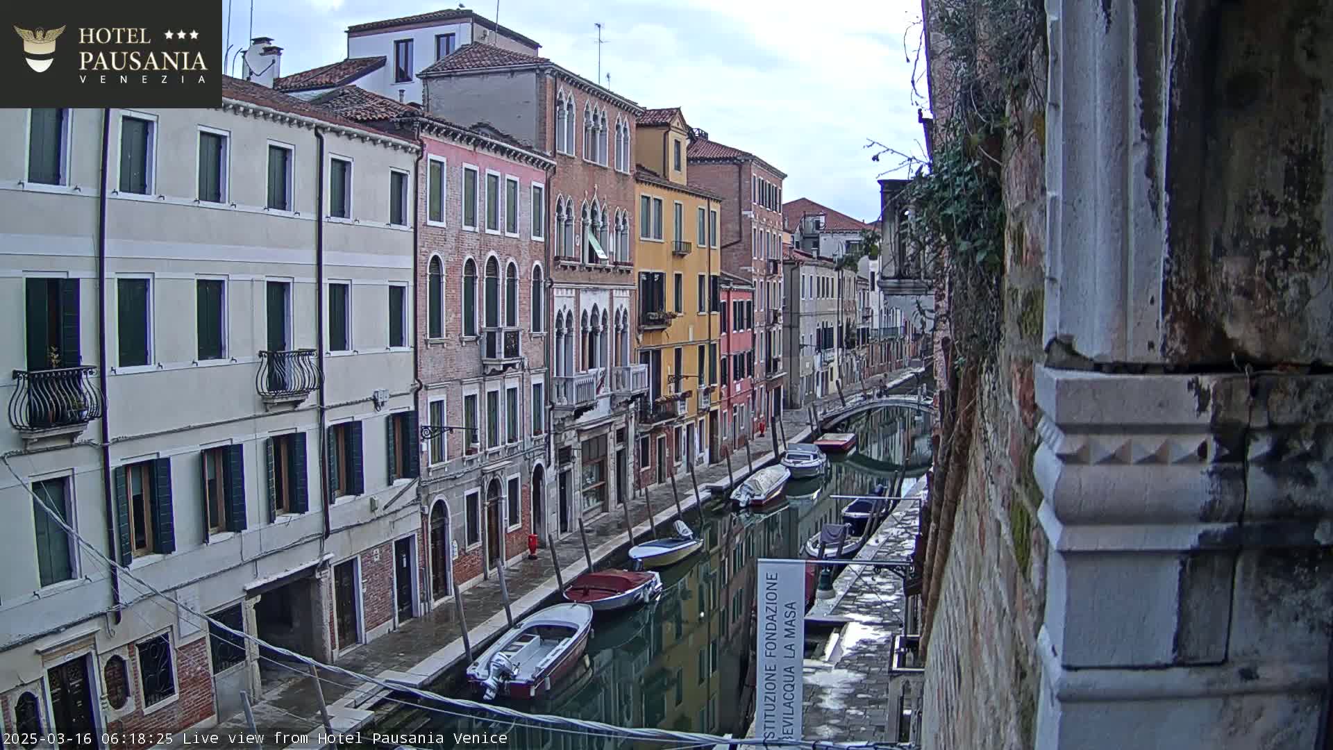 A view of a canal in Venice, Italy, showing several boats moored along the sides of colorful buildings on an overcast day.