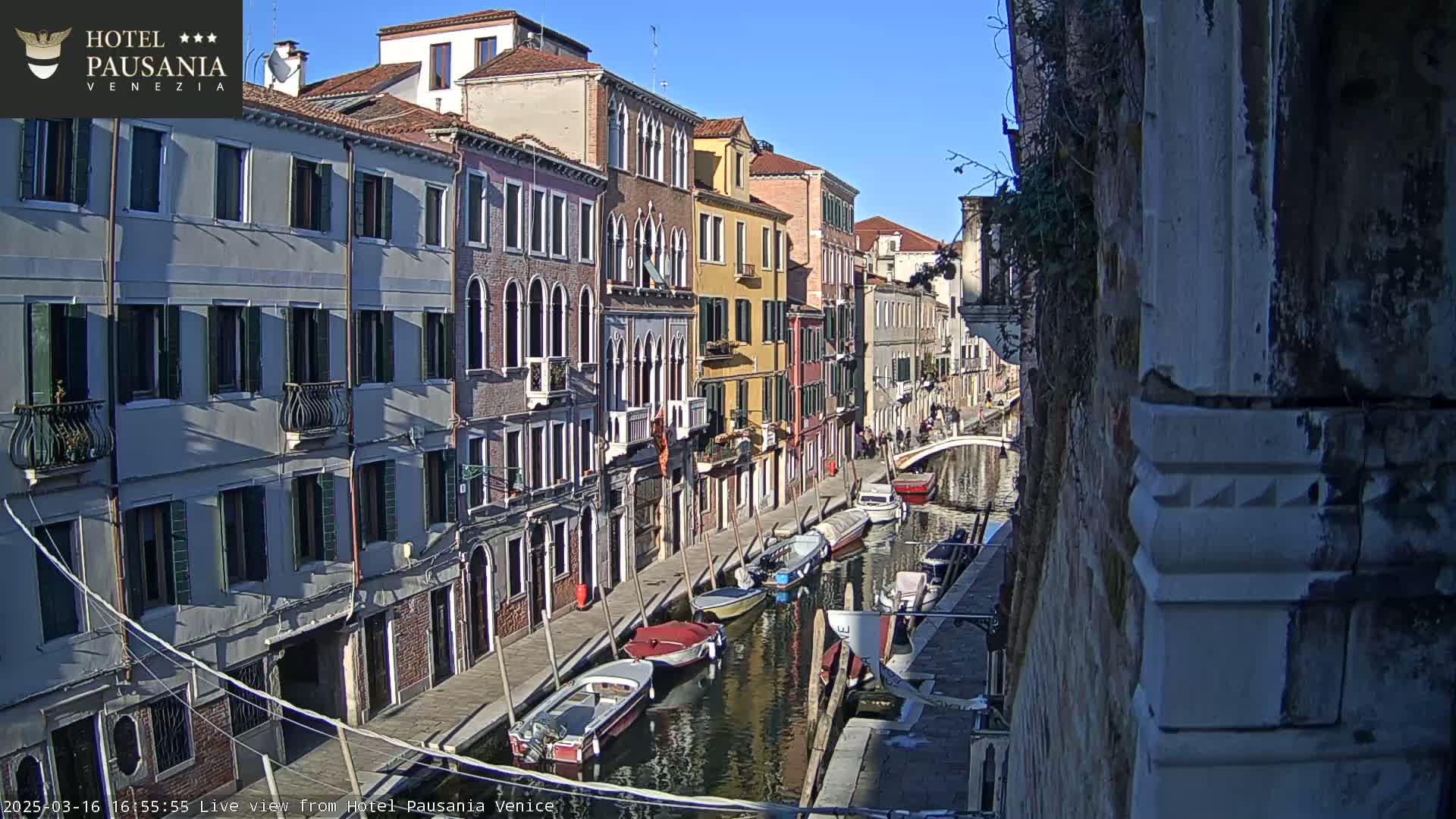 A sunny day in Venice shows several colorful buildings lining a canal where several boats are moored.