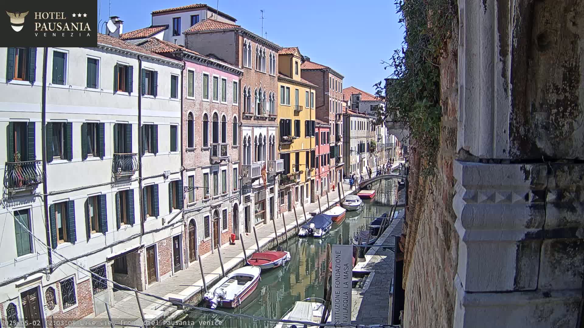 A sunny day reveals a Venetian canal lined with colorful buildings and several boats moored along its banks.