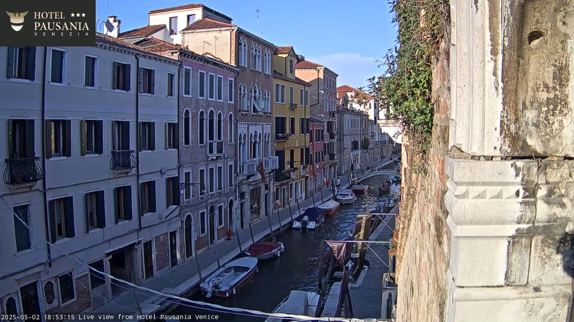 A sunny Venetian canal is lined with colorful buildings and several moored boats.