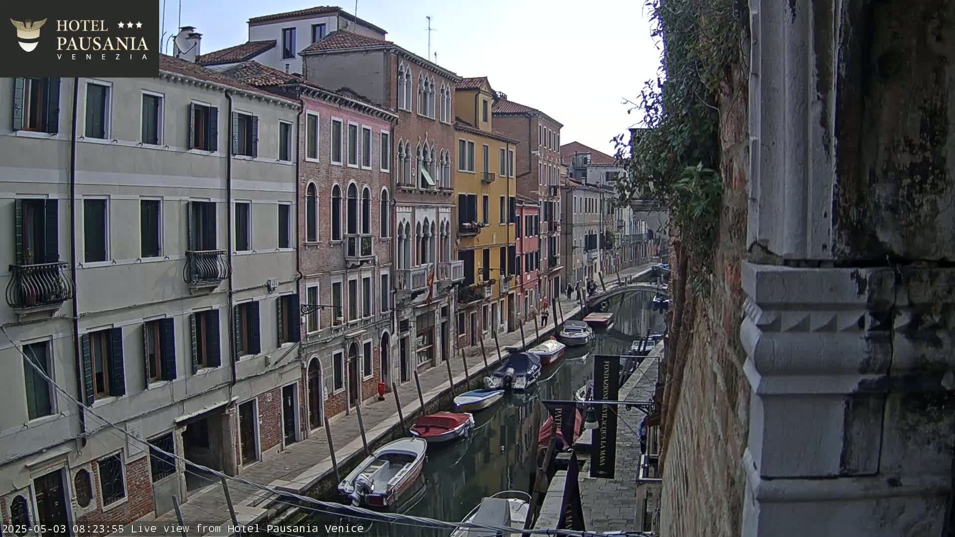 A canal in Venice, under a partly cloudy sky, is lined with colorful buildings and several moored boats.