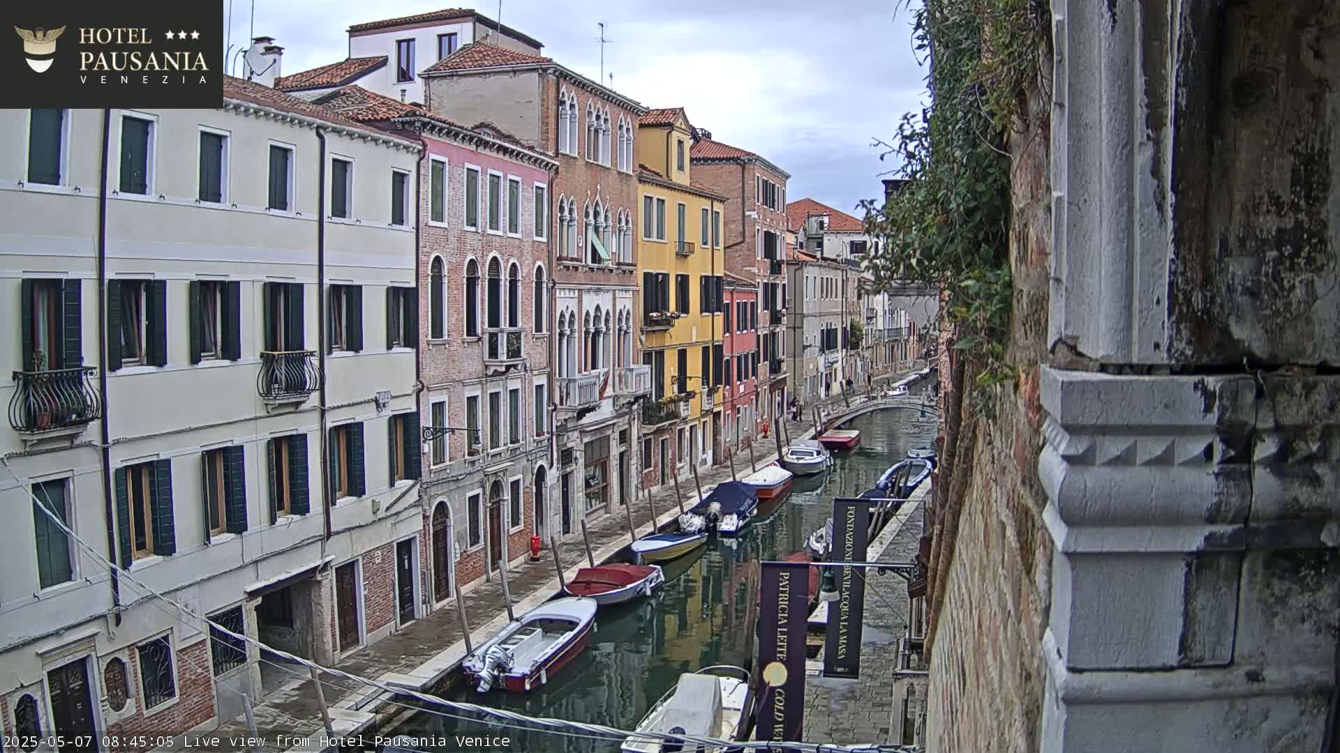 A canal in Venice, under an overcast sky, is lined with colorful buildings and several moored boats.