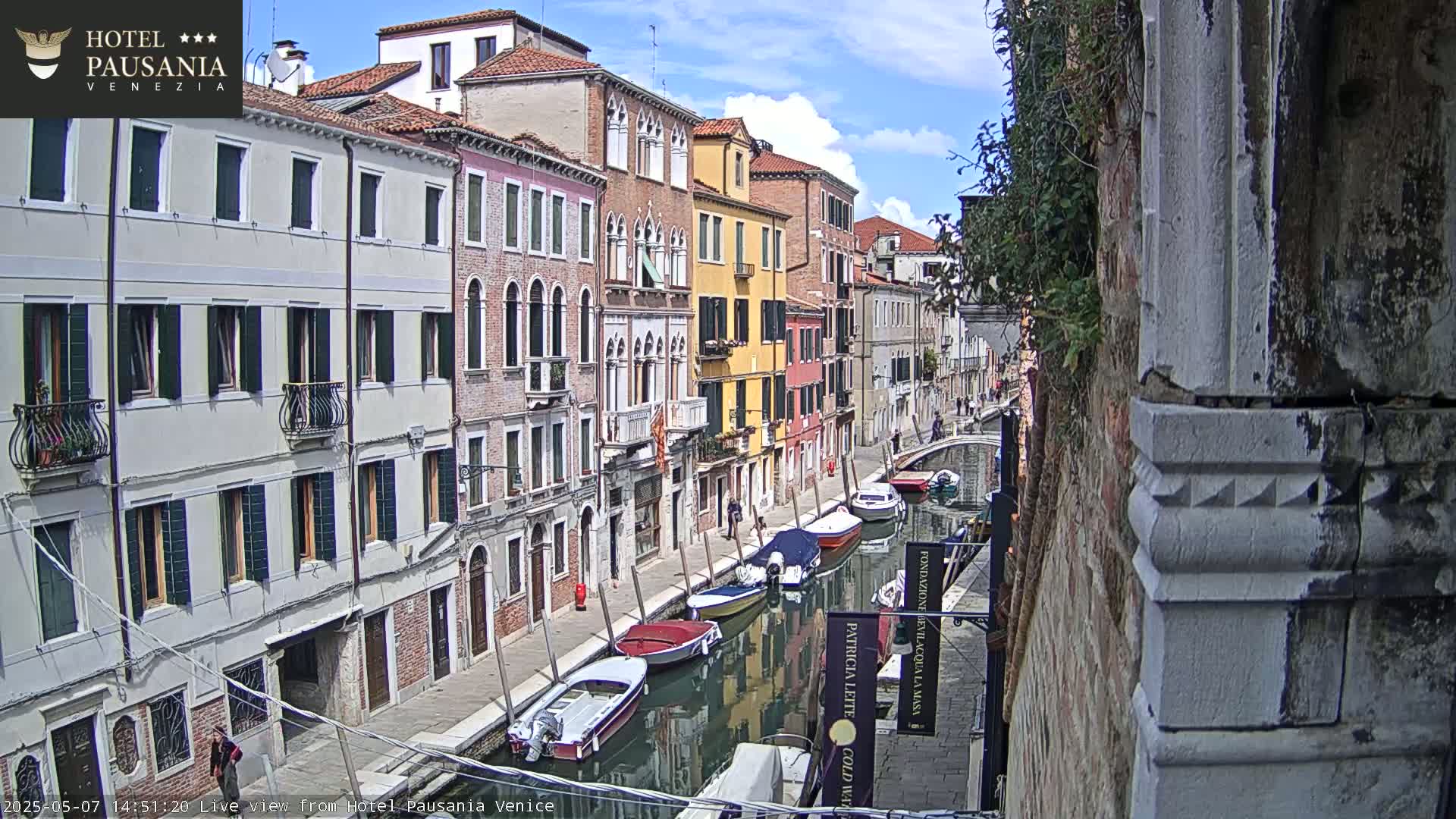 A sunny day in Venice shows a narrow canal lined with colorful buildings and several boats moored along its banks.