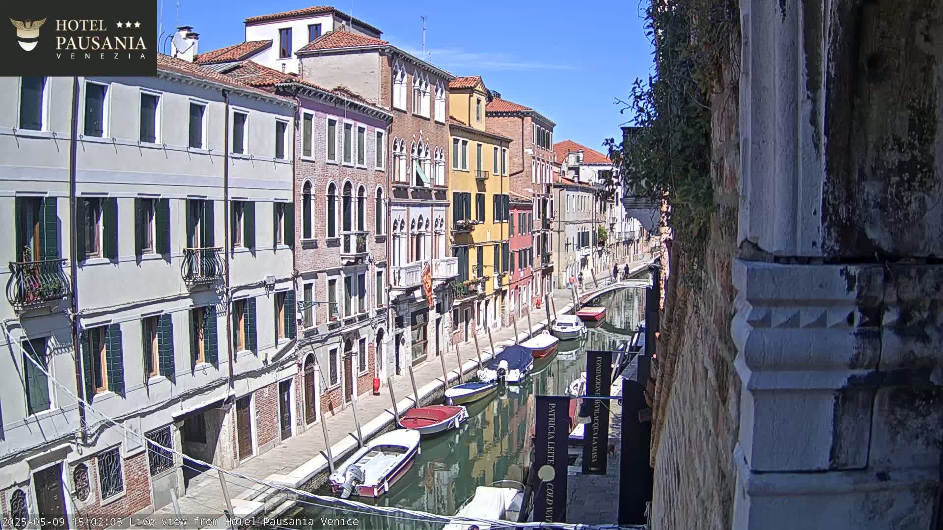 A sunny day in Venice shows colorful buildings lining a canal where several boats are moored.