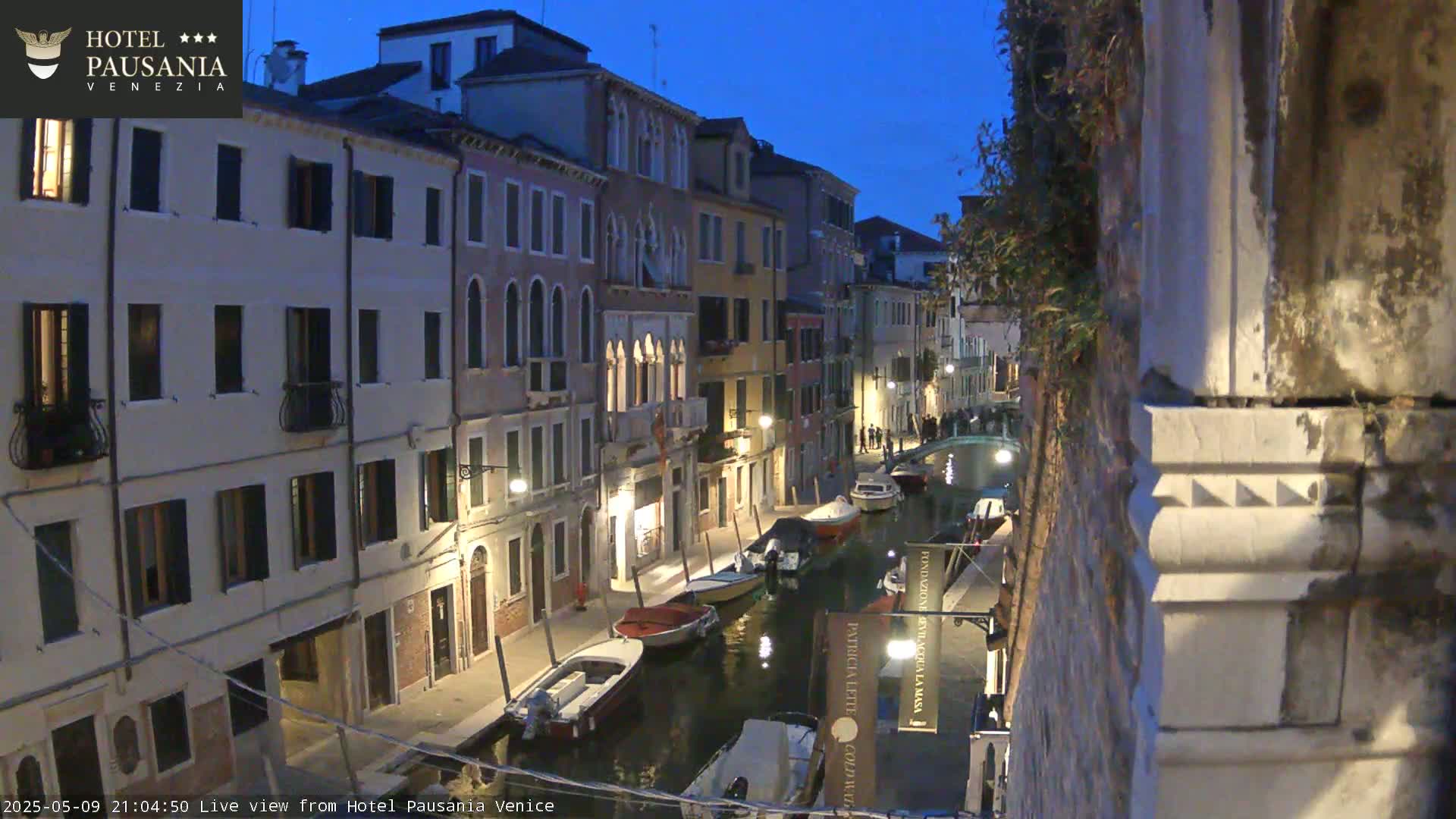 A twilight view of a narrow Venetian canal lined with buildings, several boats moored along its banks.