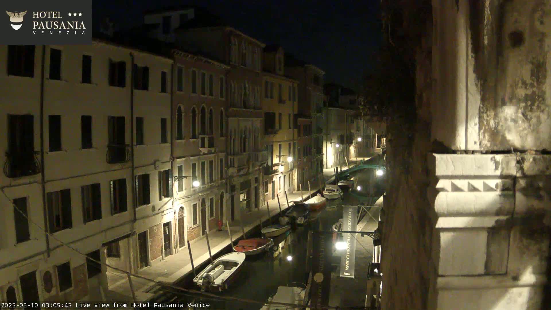A nighttime view of a narrow canal in Venice, lined with buildings and several moored boats.