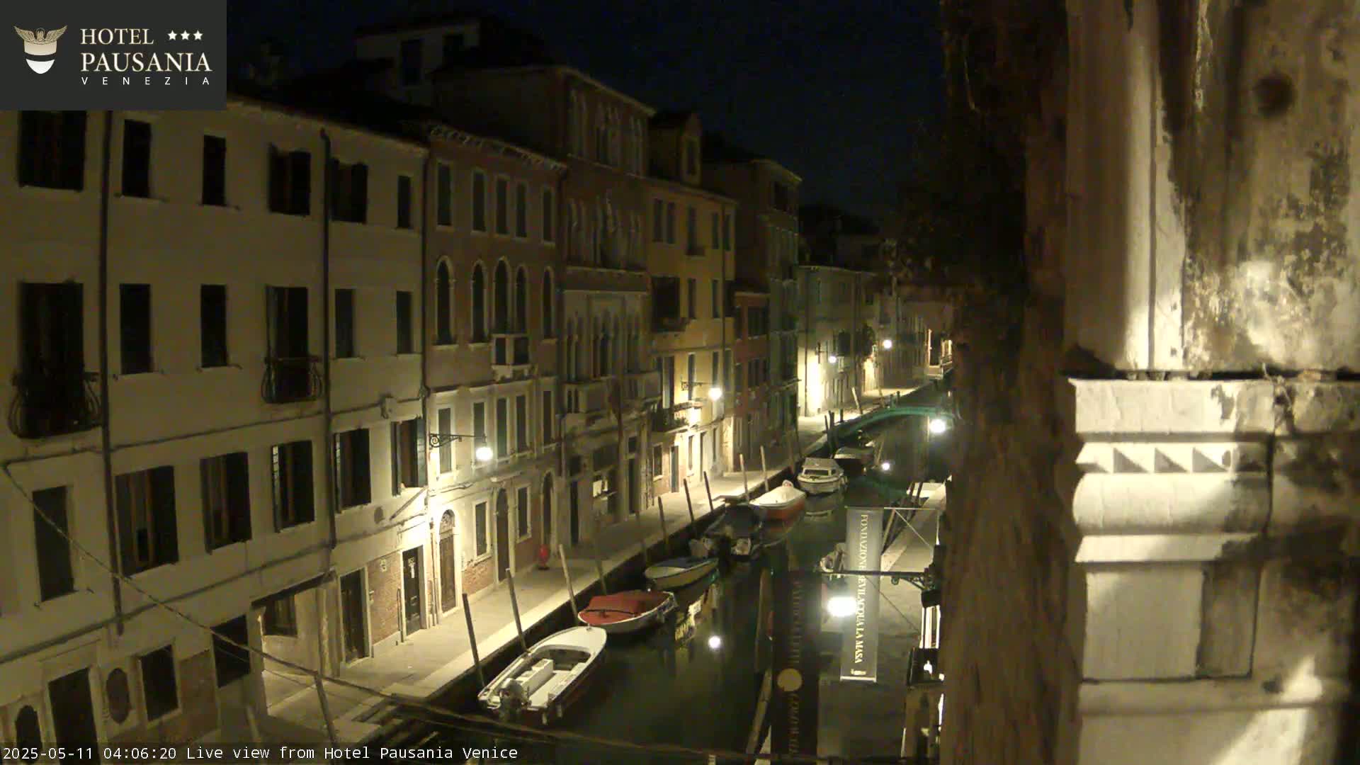 At night, several boats are moored along a canal lined with illuminated buildings.