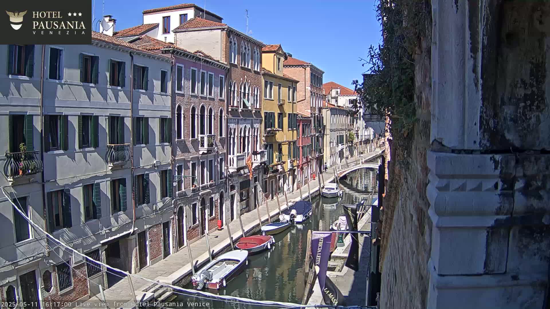 A sunny day in Venice shows several boats moored along a narrow canal beside colorful buildings.