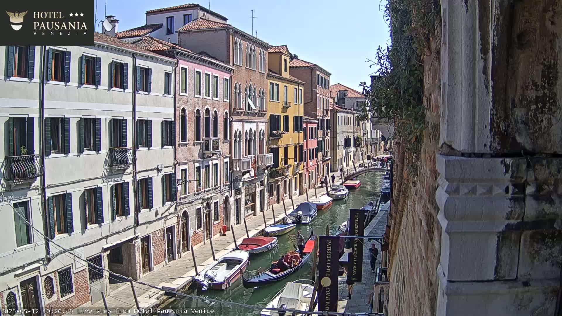A sunny day in Venice shows a narrow canal lined with colorful buildings and several boats, including a gondola.