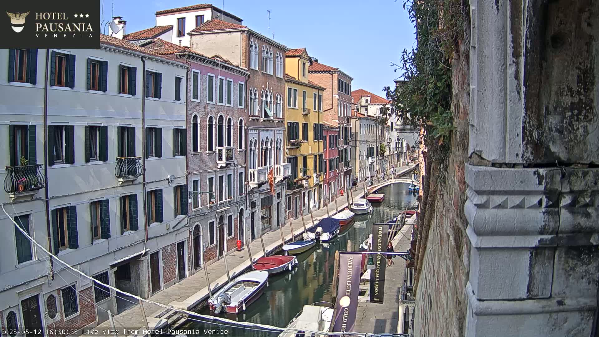 A sunny view of a canal in Venice, Italy, lined with colorful buildings and several moored boats.
