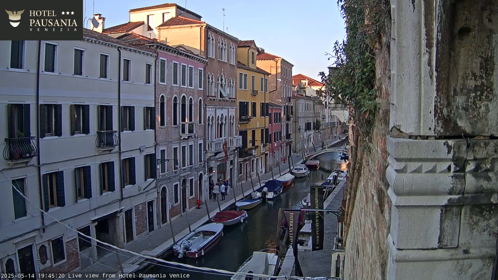 Several colorful buildings line a canal in Venice at dusk, with several small boats moored along its edge.
