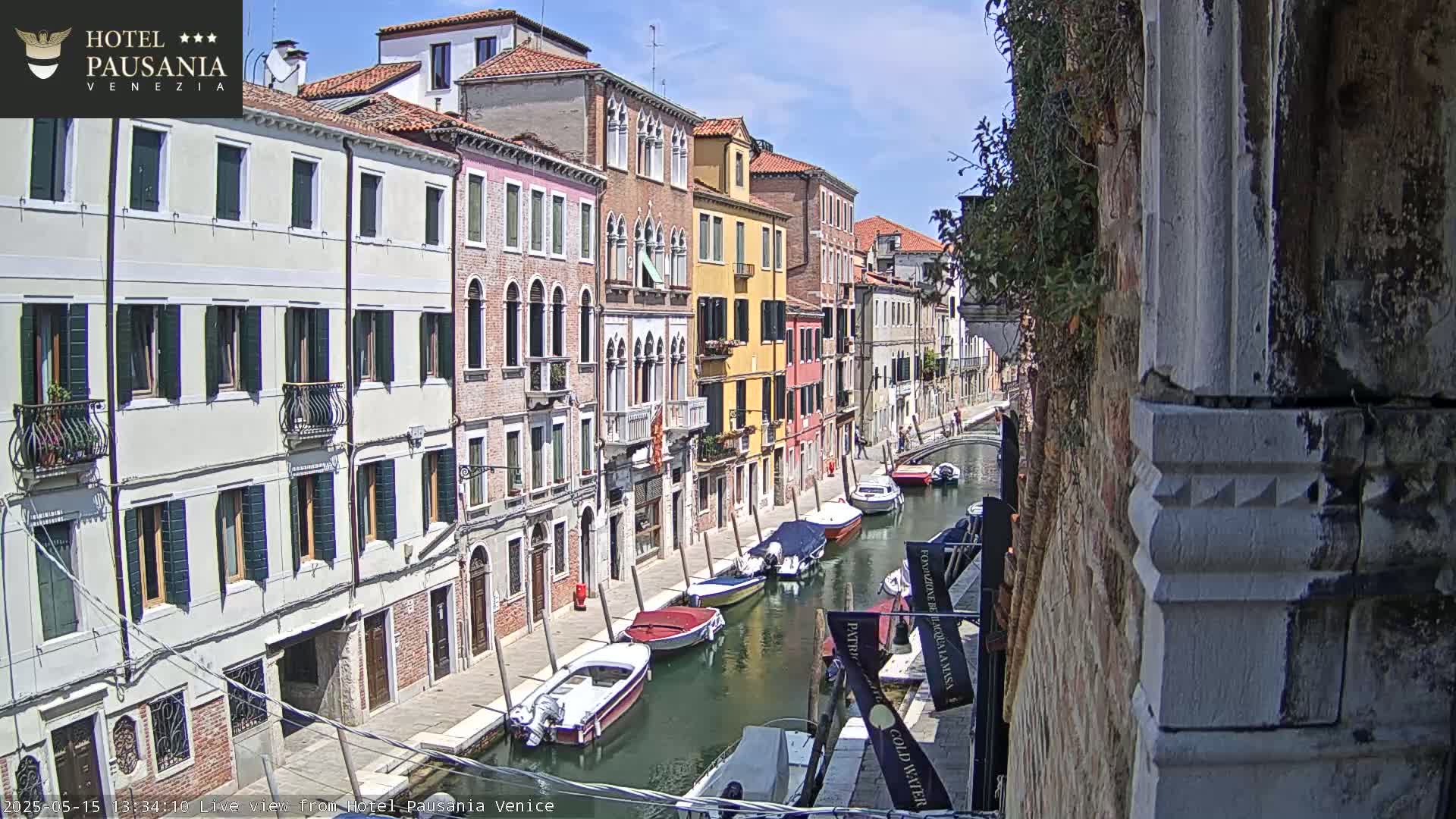 A sunny day in Venice shows colorful buildings lining a canal with several boats moored along the waterway.
