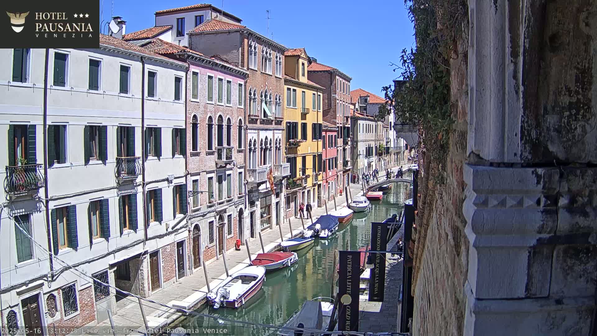 A sunny day in Venice shows colorful buildings lining a canal with several motorboats moored along its edge.
