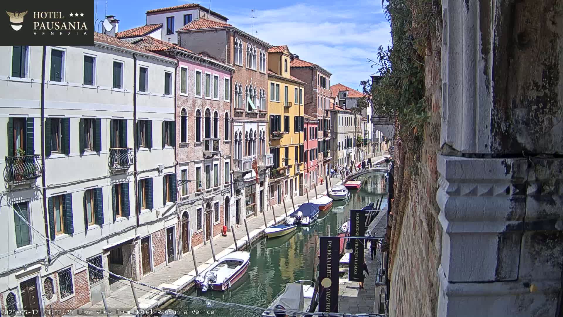 A sunny day in Venice shows a narrow canal lined with colorful buildings and several boats moored along its banks.