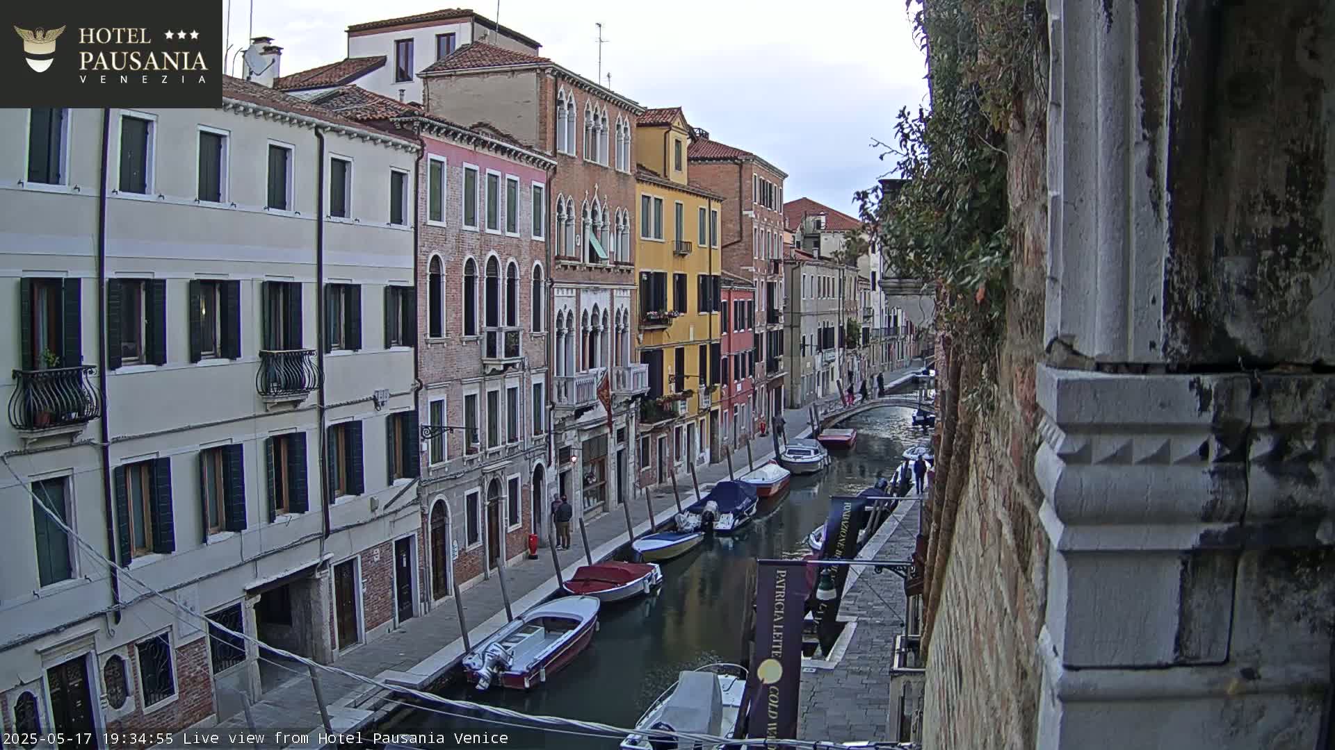 A canal in Venice, under an overcast sky, is lined with colorful buildings and several moored motorboats.