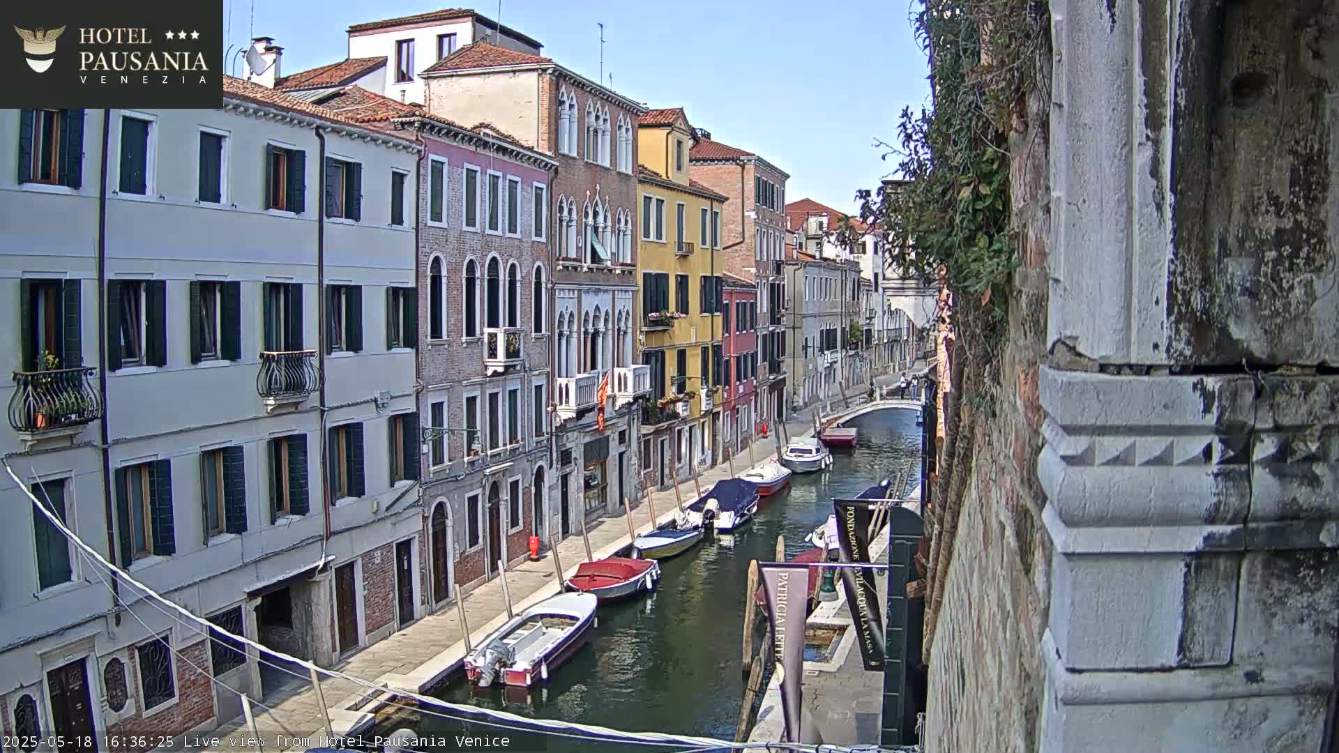 A sunny day in Venice shows several boats moored along a narrow canal lined with colorful buildings.