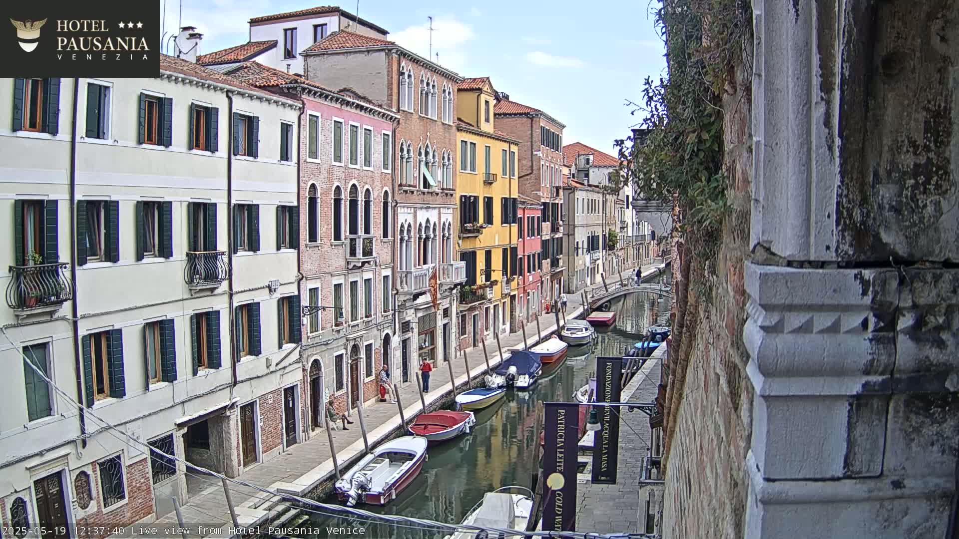 A sunny day in Venice shows a canal lined with colorful buildings and several moored boats.