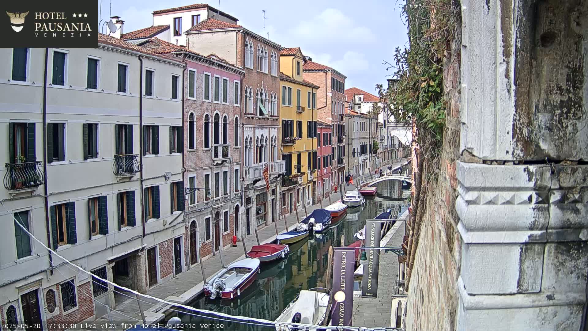 A canal in Venice, under a partly cloudy sky, is lined with colorful buildings and several moored motorboats.