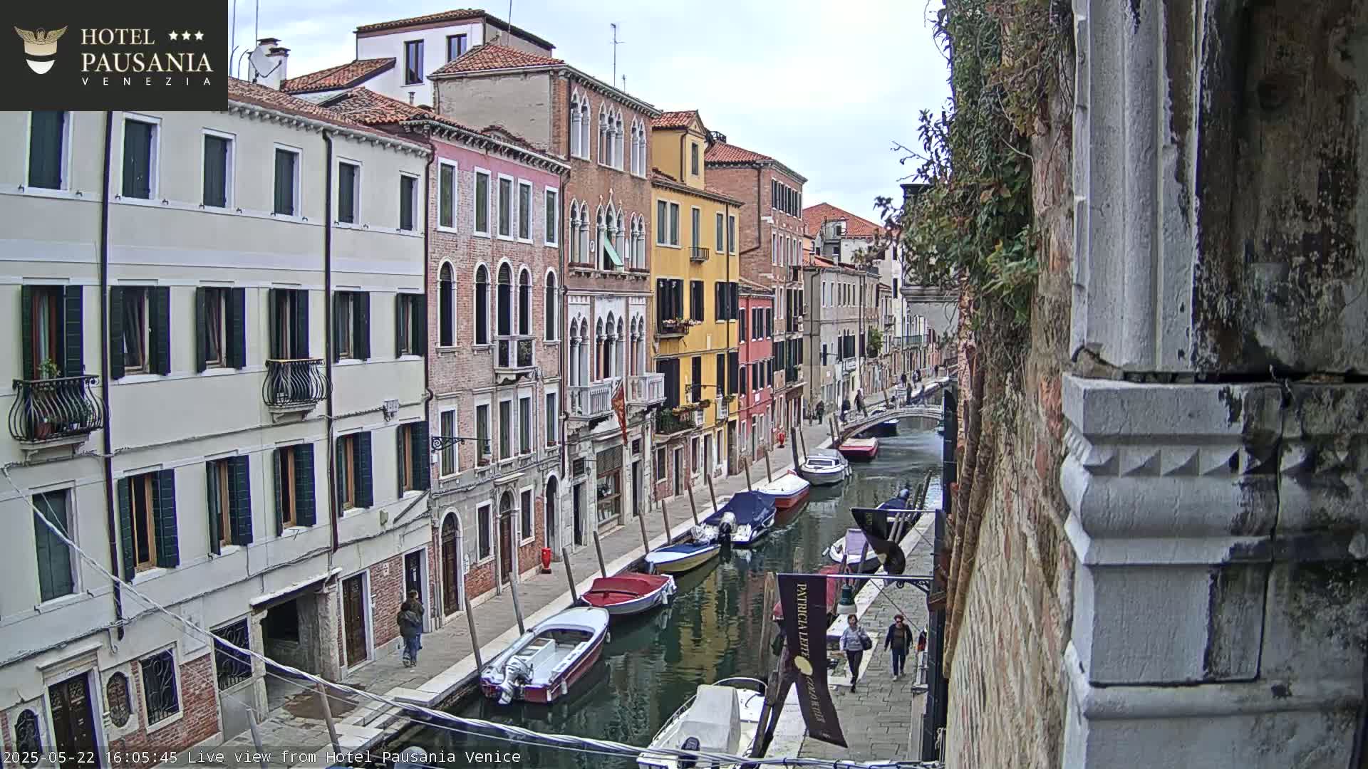 A canal in Venice, Italy, with colorful buildings lining its banks, several small boats moored along the waterway, and overcast skies.