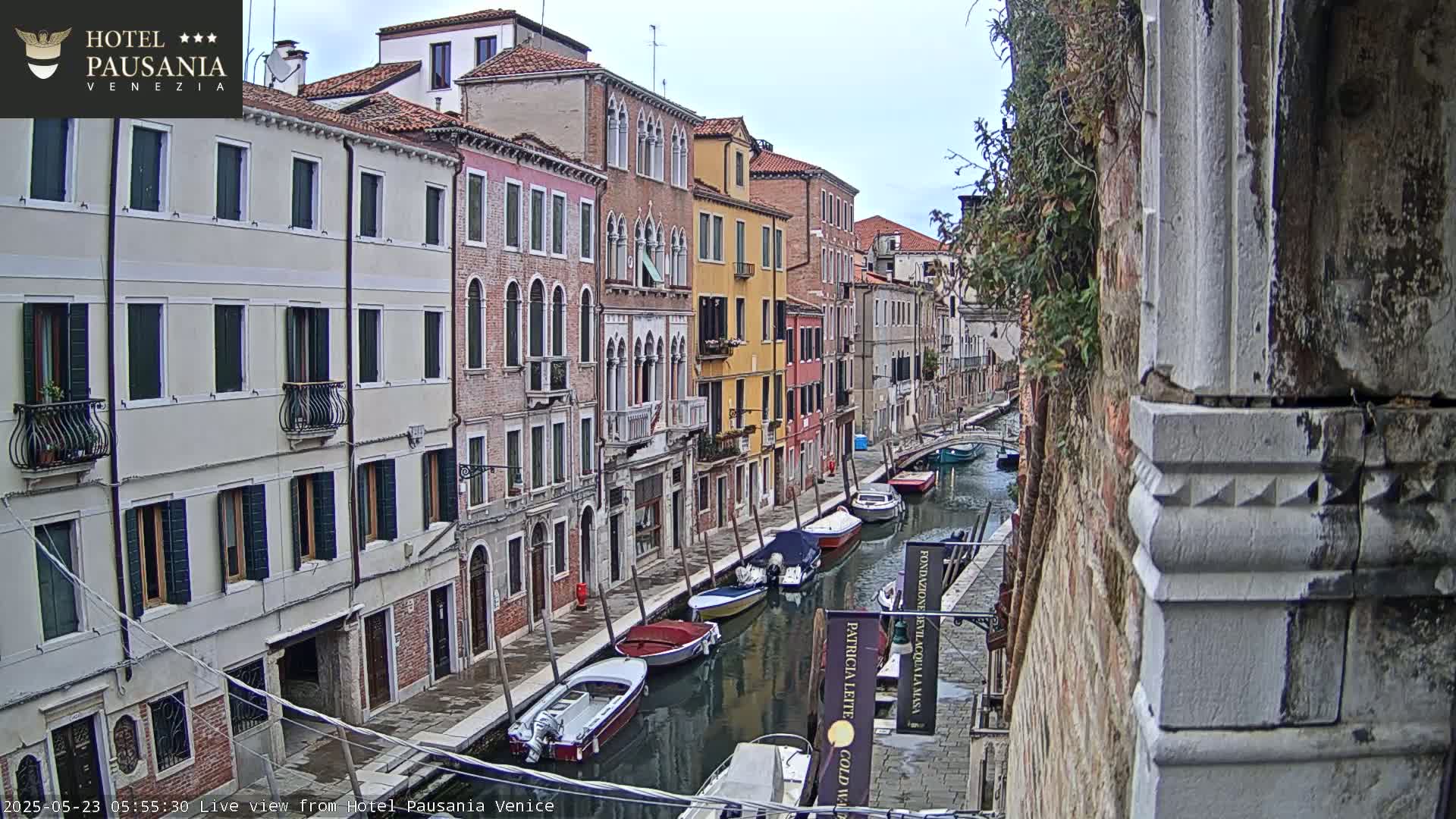 A canal in Venice, Italy, with several boats moored along its banks, is viewed from a slightly elevated position on an overcast day.