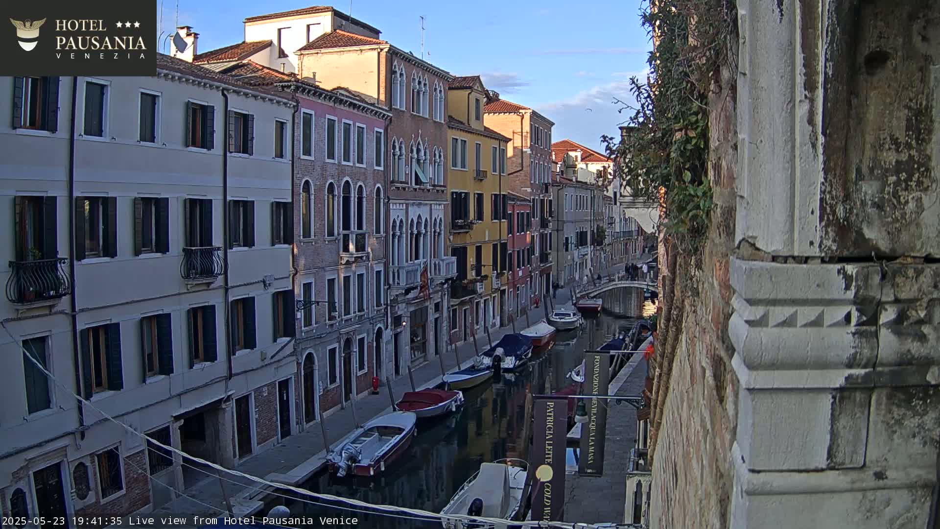 A narrow canal in Venice, under a clear evening sky, is lined with colorful buildings and several moored boats.