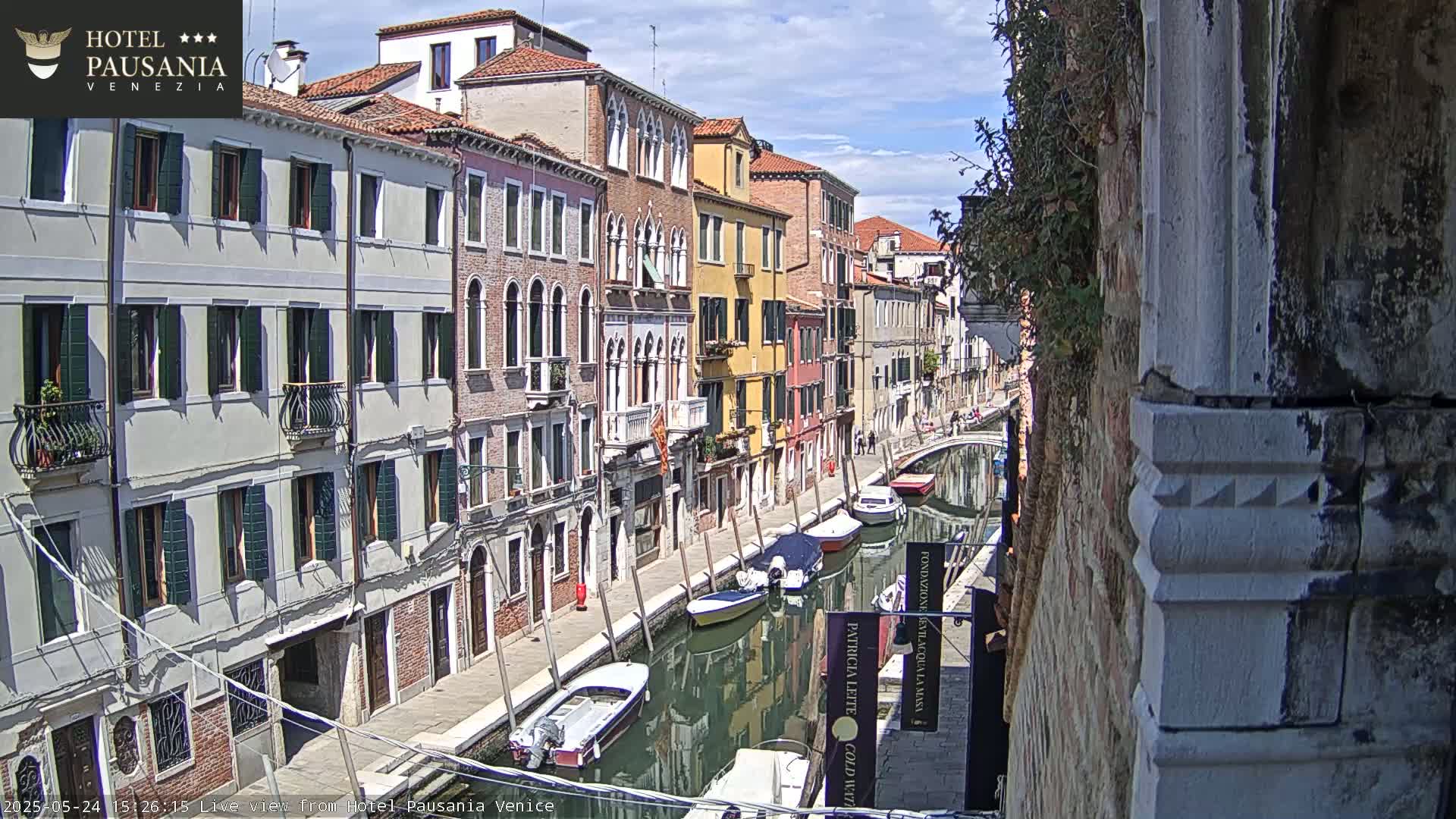 A sunny day in Venice shows a canal lined with colorful buildings and several moored boats.