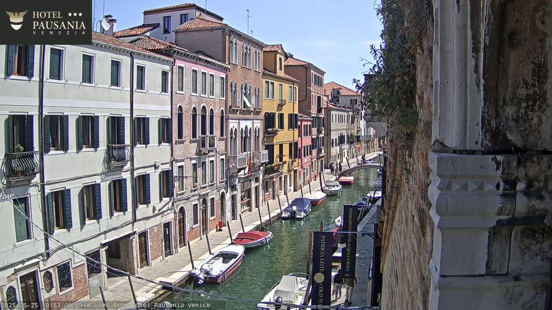 A sunny day in Venice shows a canal lined with colorful buildings and several moored motorboats.
