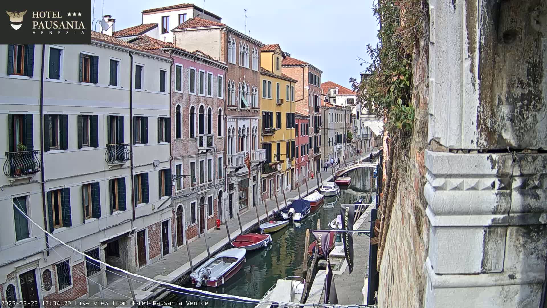 Several colorful buildings line a canal in Venice, with several boats moored along the waterway on a sunny day.